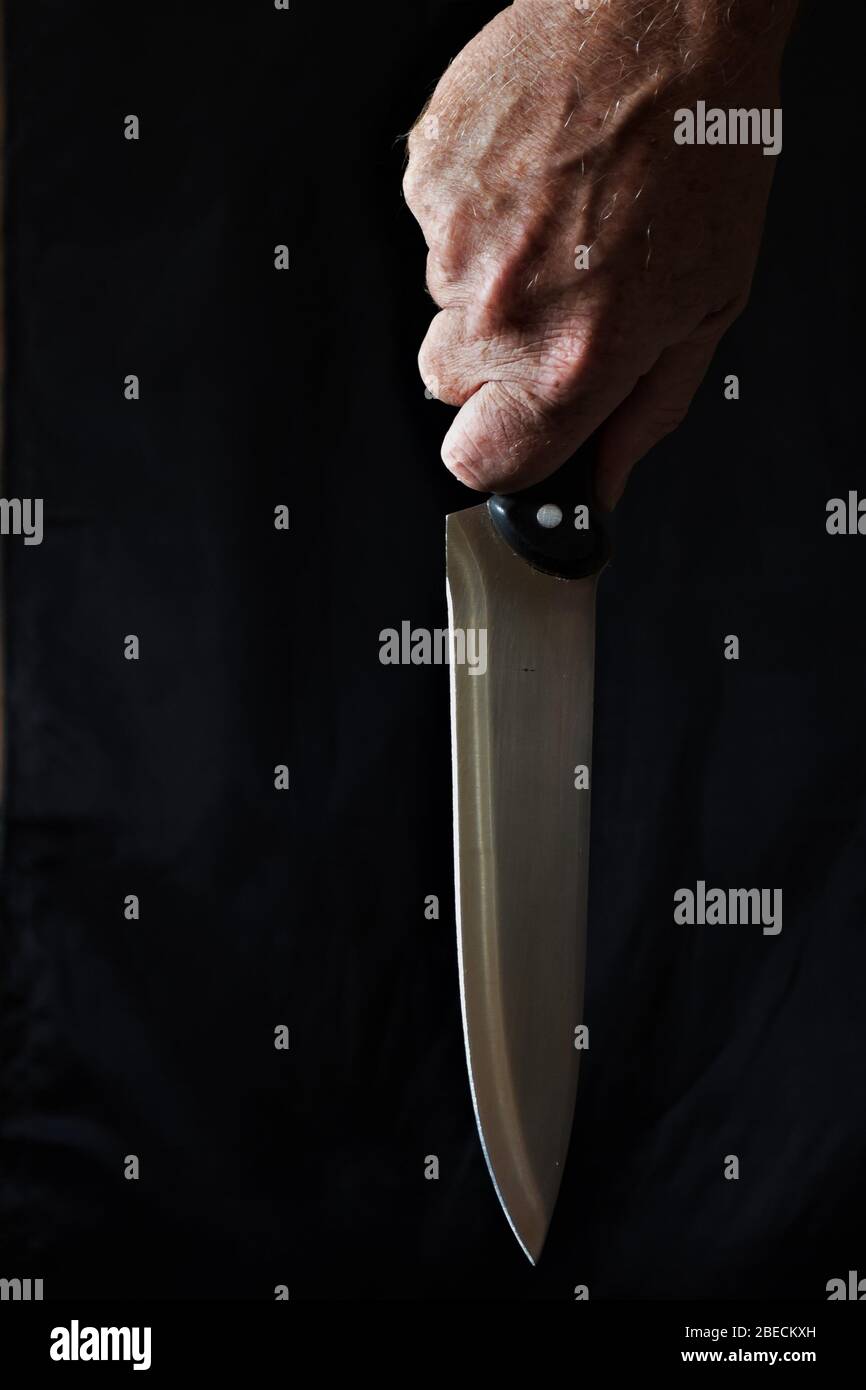 close up of hand holding a kitchen carving knife against a black background Stock Photo