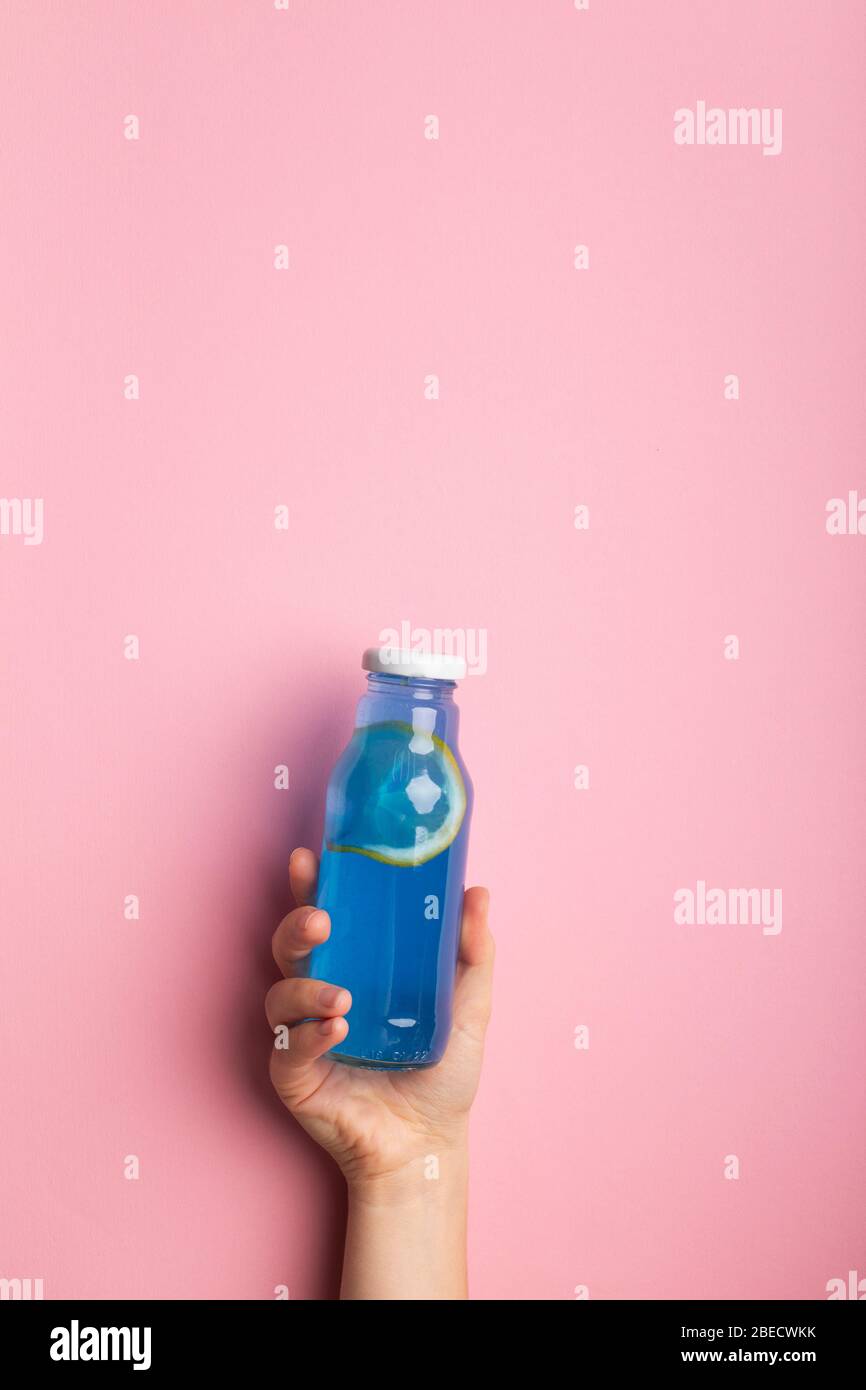 Blue detox water with lemon slice in woman hand on pink Stock Photo