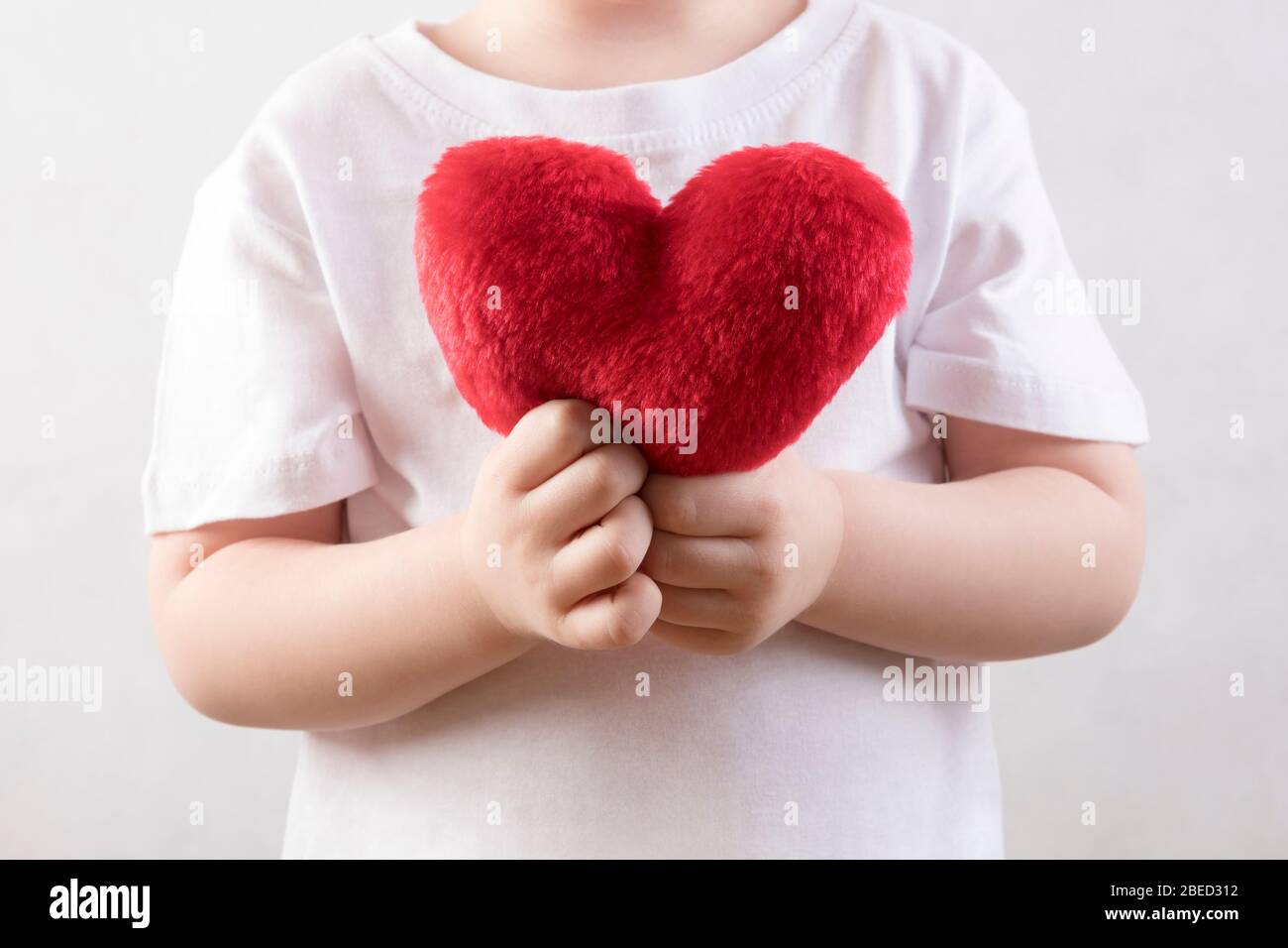 Three year old child holding a fluffy red heart Stock Photo