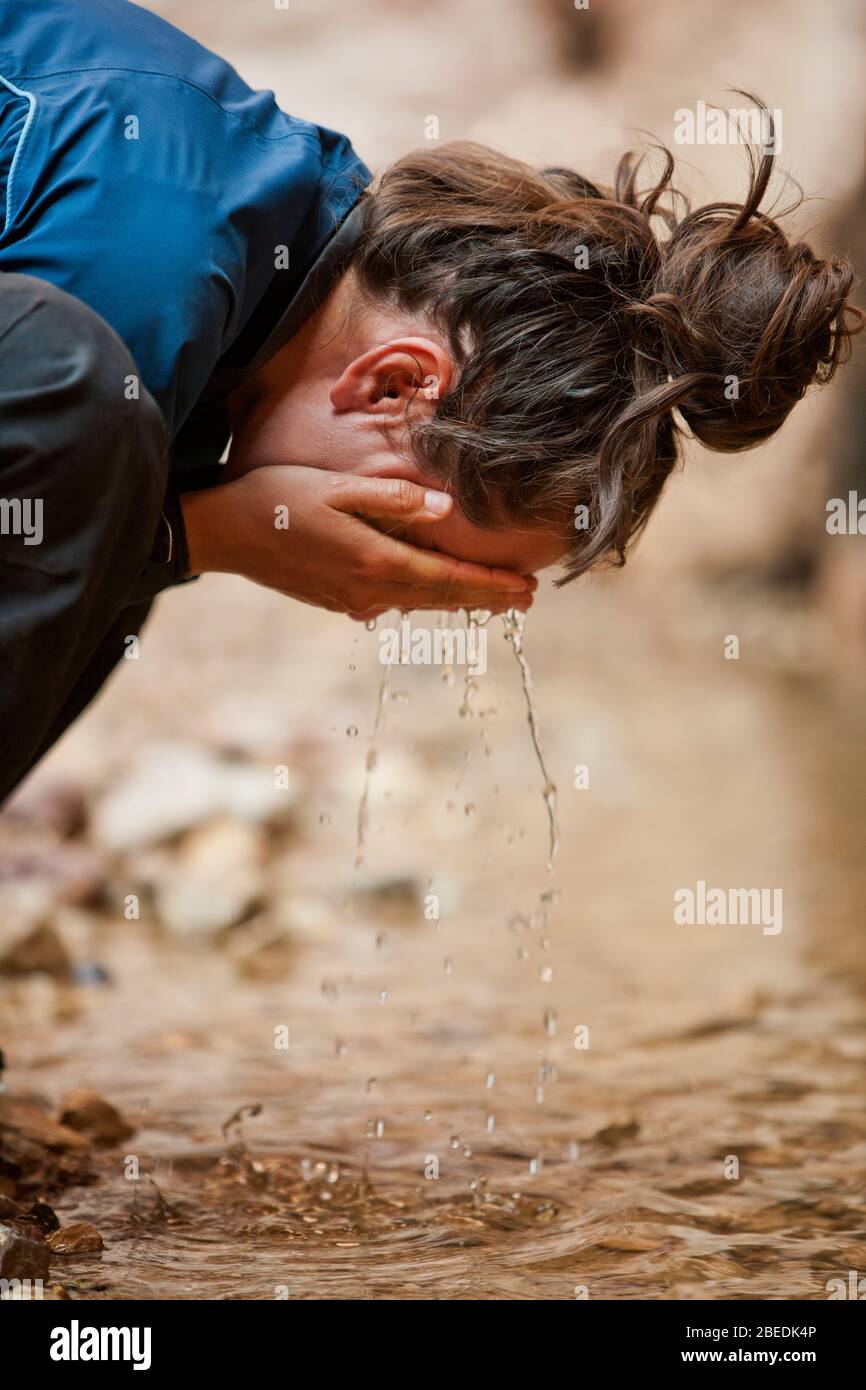 Young woman splashing water from a stream onto her face. Stock Photo