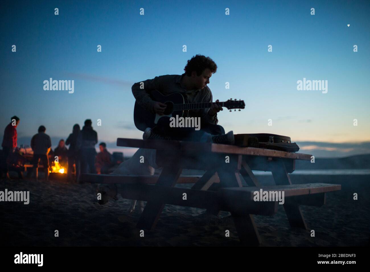 Teenage boy playing guitar on a picnic table at the beach at sunset Stock Photo