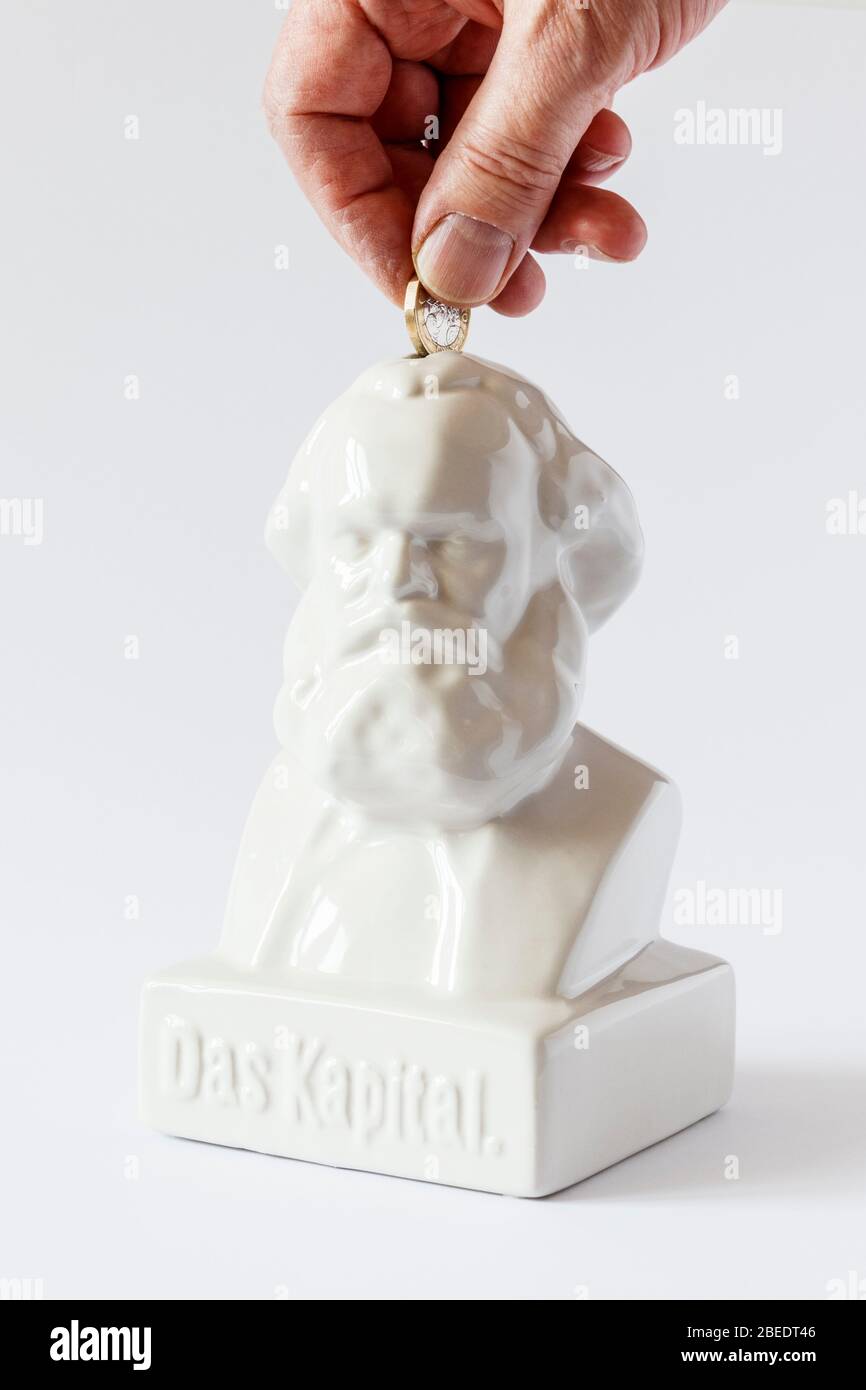 Male hand inserting a one-pound coin into a white ceramic money box in the shape of a bust of the German philosopher Karl Marx, labelled 'Das Kapital' Stock Photo