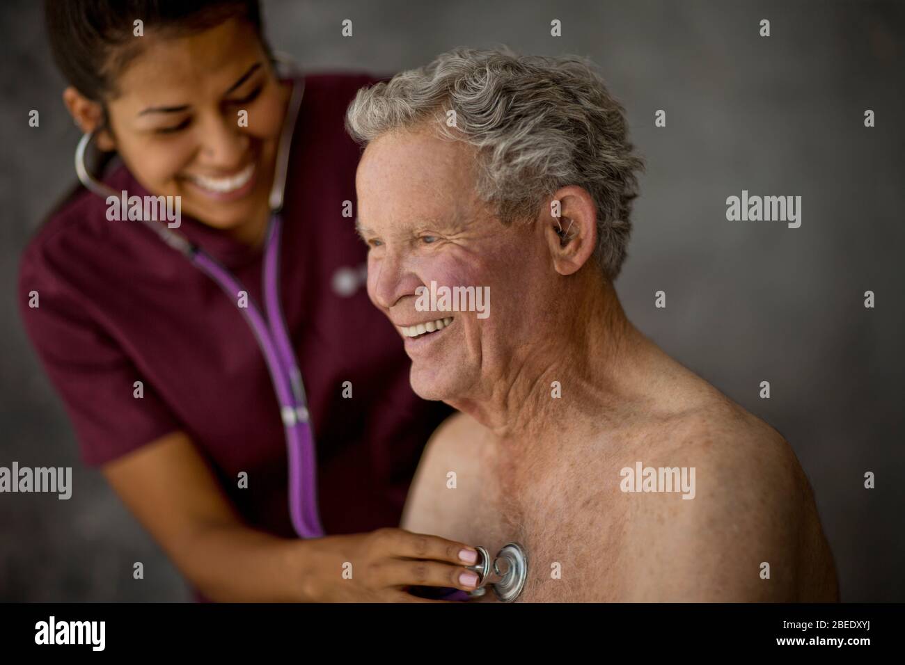 Smiling young nurse listening to a senior patient's heartbeat Stock Photo