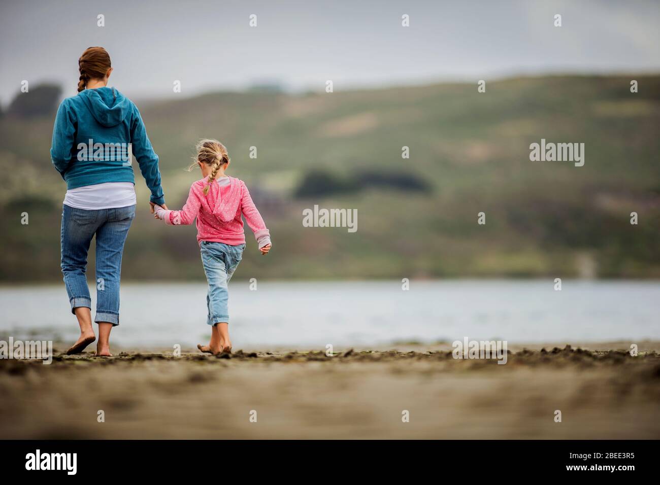 Young blonde girl walking hand-in-hand with her mother along the beach Stock Photo