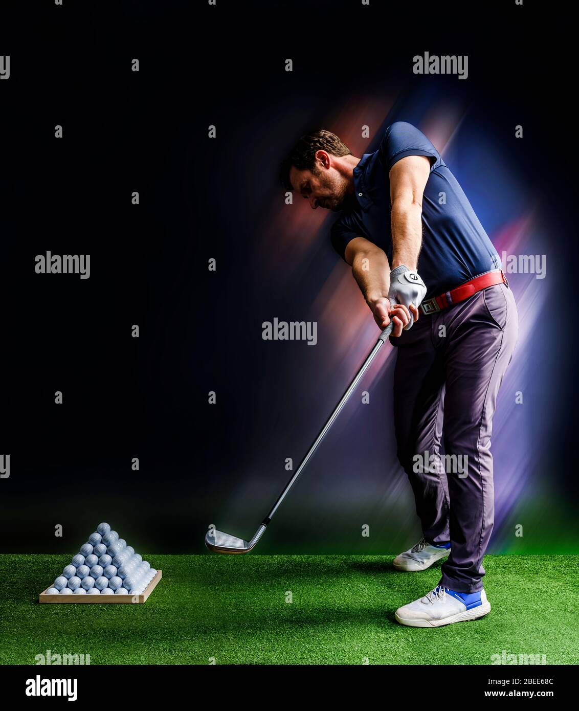 Golf player practicing in a driving range with pyramid of golf balls