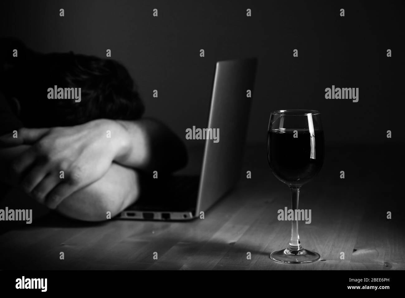 Home office and alcoholism problem - depressed man sitting in front of computer, he hide his face. Wine glass on the table Stock Photo