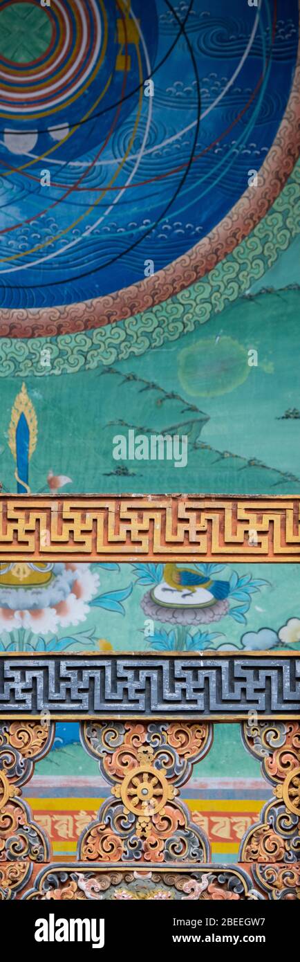 Bhutan, Punakha Dzong. Traditional hand painted and carved wooden architectural detail in front of colorful mural. Stock Photo