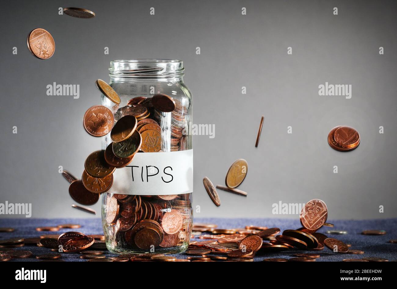 Coins falling on a tips money jar full of UK Sterling Stock Photo