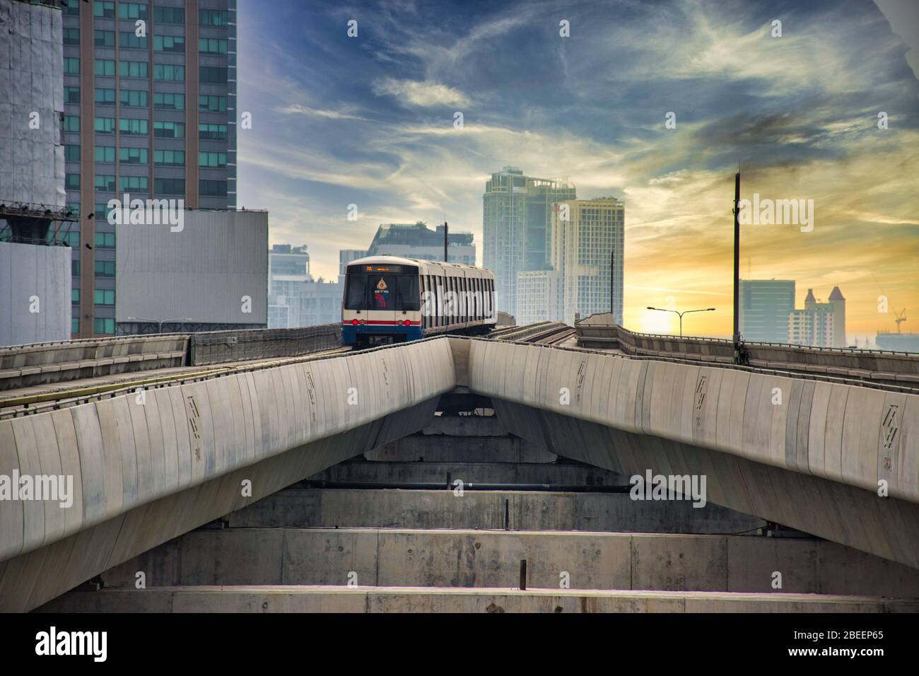 Bangkok, Thailand 04.11.2020: Skytrain is leaving the Ratchayothin BTS station on the Sukhumvit Line towards the blue and yellow sunset Stock Photo