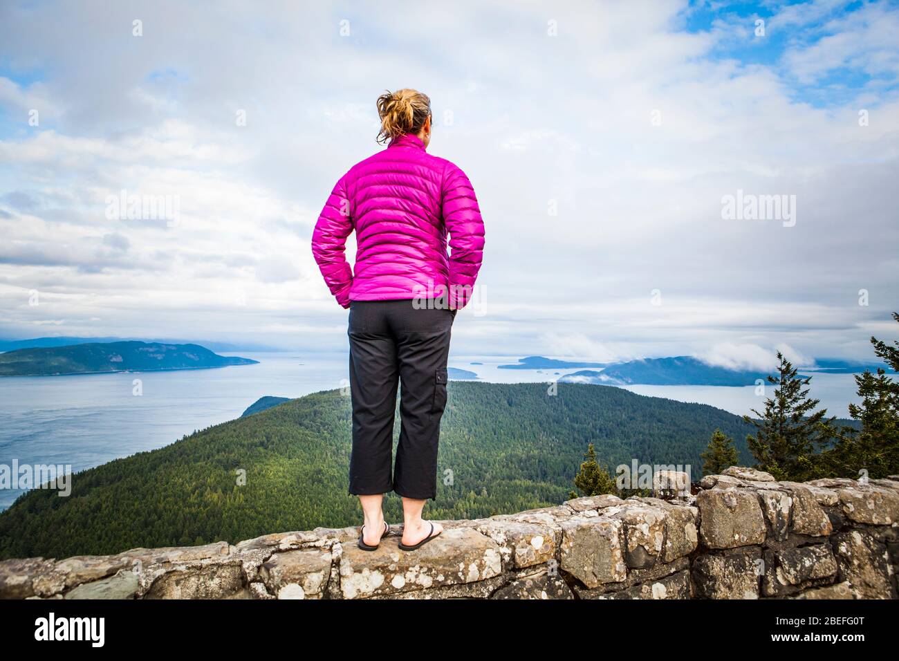 A woman standing atop a rock wall at the top of Mount Constitution in Moran State Park, Orcas Island, Washington, USA. Stock Photo
