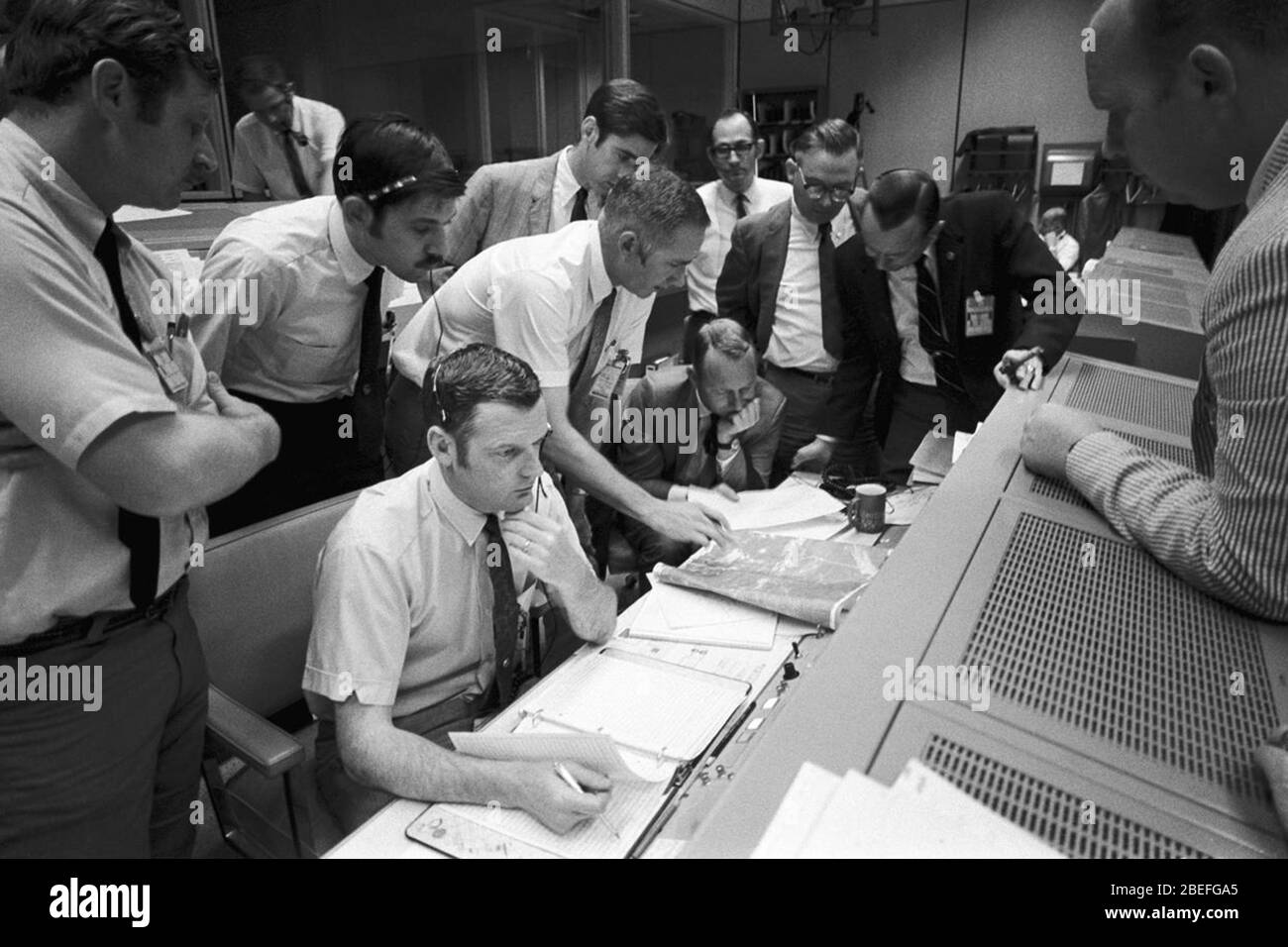 A group of flight controllers gathers around the console of Glynn S. Lunney (seated, nearest camera), Shift 4 flight director, in the Mission Operations Control Room (MOCR) of Mission Control Center (MCC), located in Building 30 at the Manned Spacecraft Center (MSC). Among those looking on is Dr. Christopher C. Kraft, deputy director, MSC, standing in a black suit, on the right. When this photograph was taken, the Apollo 13 lunar landing mission had been canceled, and the problem-plagued Apollo 13 crew members were in trans-Earth trajectory attempting to bring their crippled spacecraft back ho Stock Photo