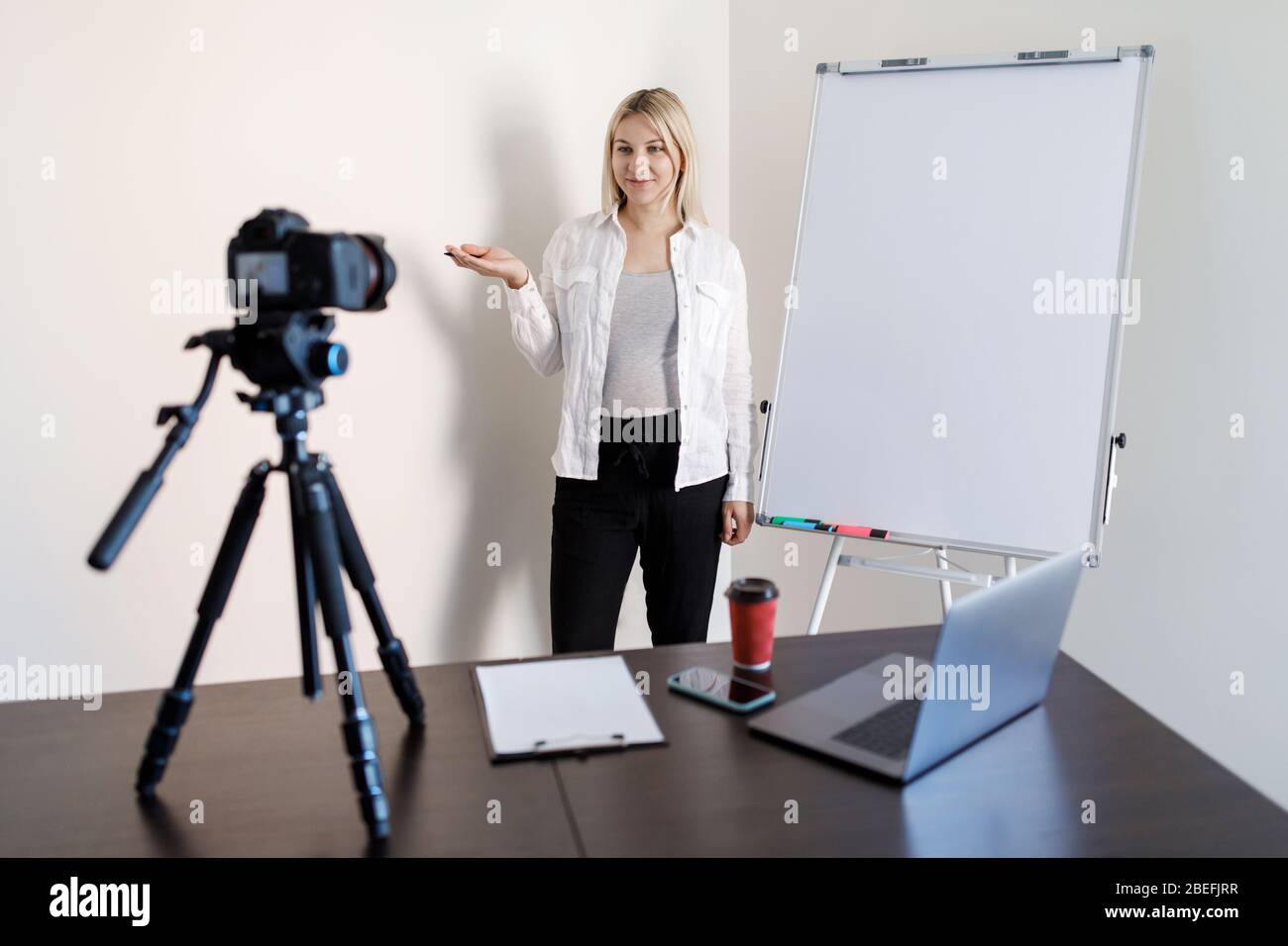 A young pregnant woman tutor records training video lessons to the camera, she stands and shows with a pen on a flip chart with graphs and diagrams Stock Photo