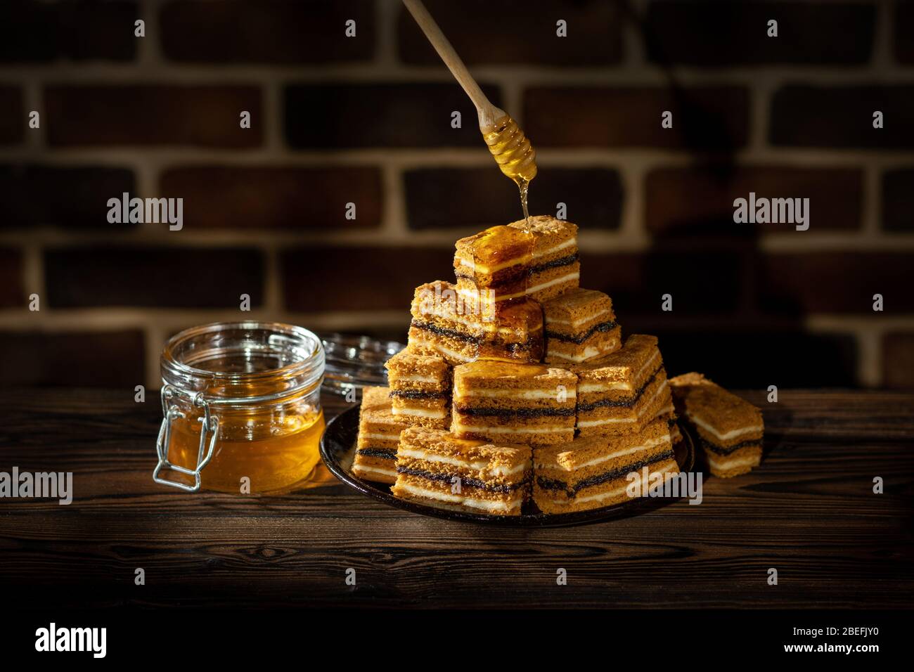 Plate with slices of honey cake and jar with honey on wooden table and brick wall background Stock Photo