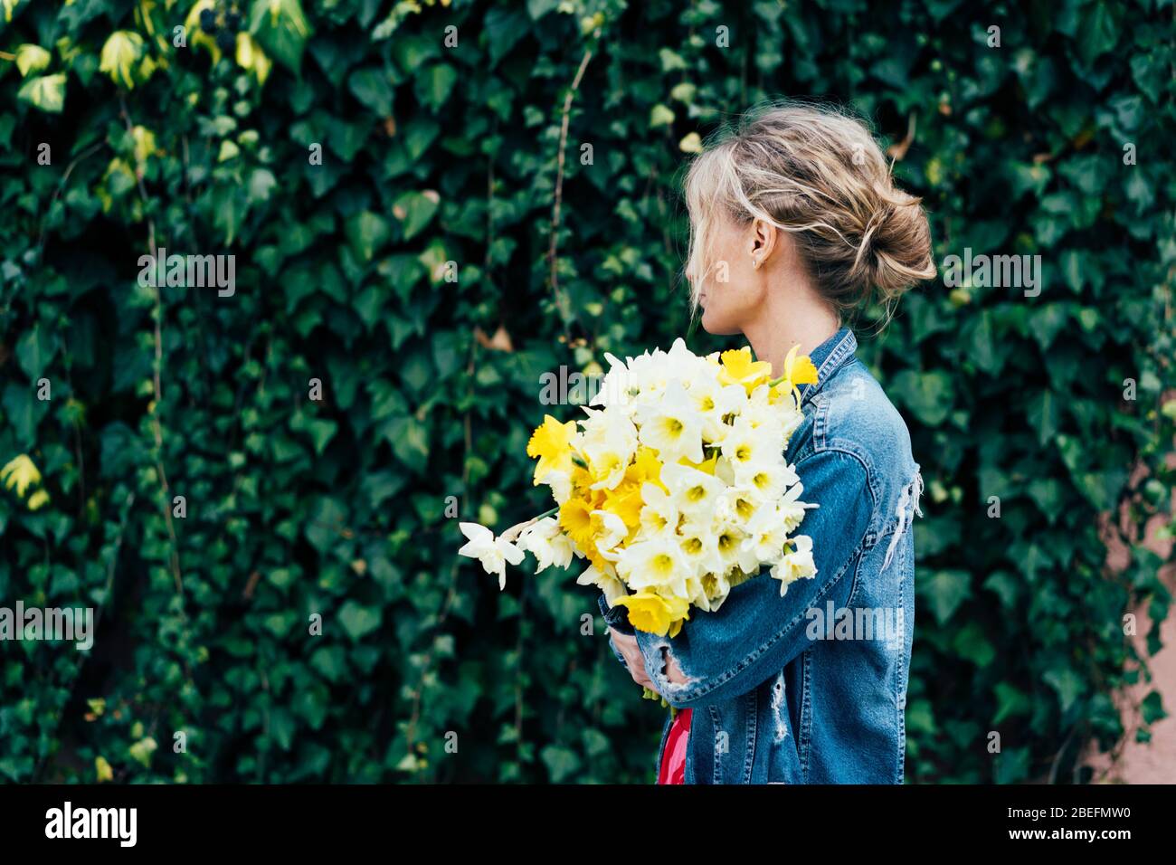 Spring content. Young charming blonde hipster with a bouquet of daffodils  Stock Photo