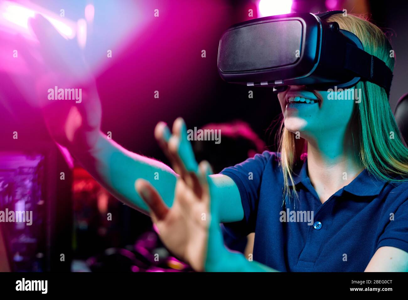 Positive girl using virtual reality simulator gesturing hands to bright ...