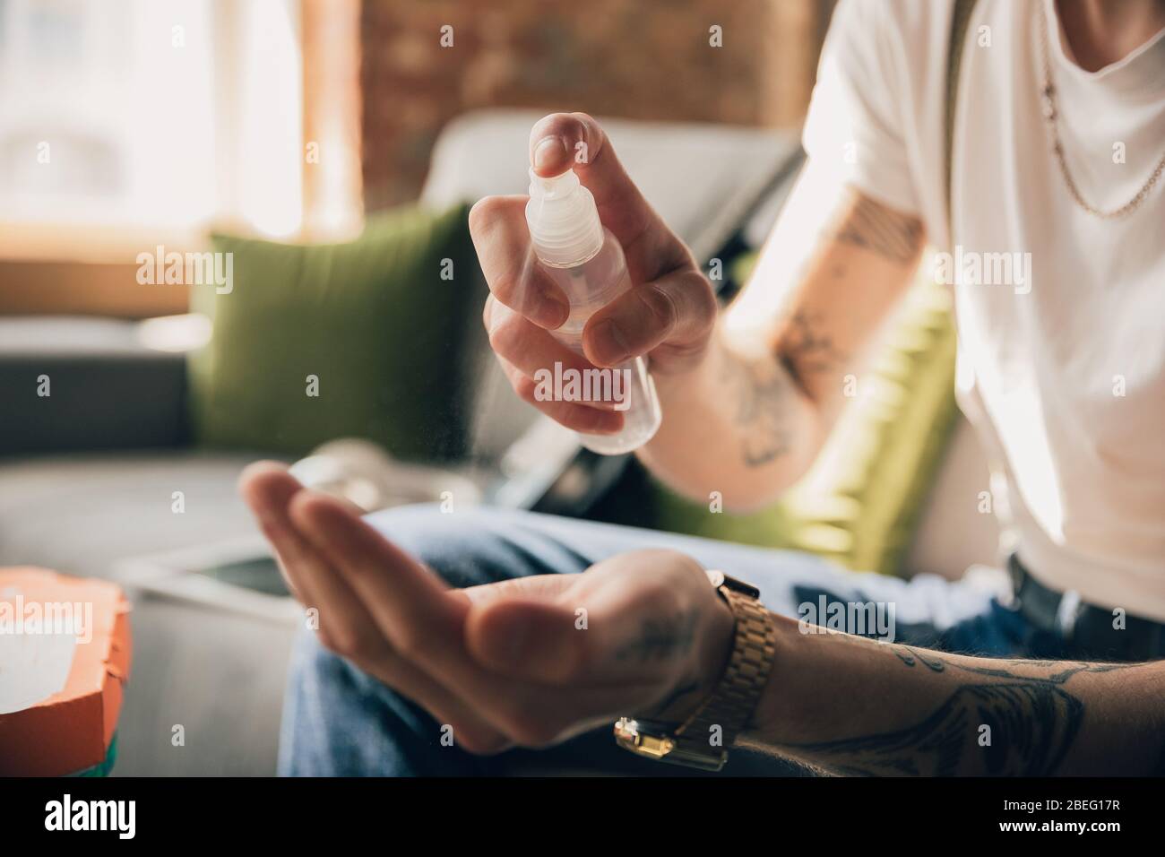 Disinfecting. Man studying at home during online courses, smart school. Getting classes or profession while isolated, quarantine against coronavirus spreading. Using laptop, smartphone, headphones. Stock Photo