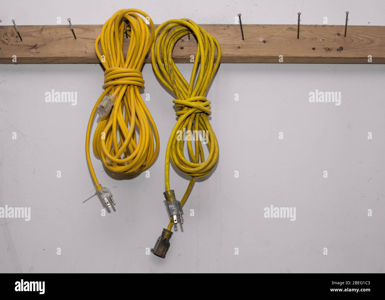 Two yellow electrical extension cords hanging in a workshop Stock