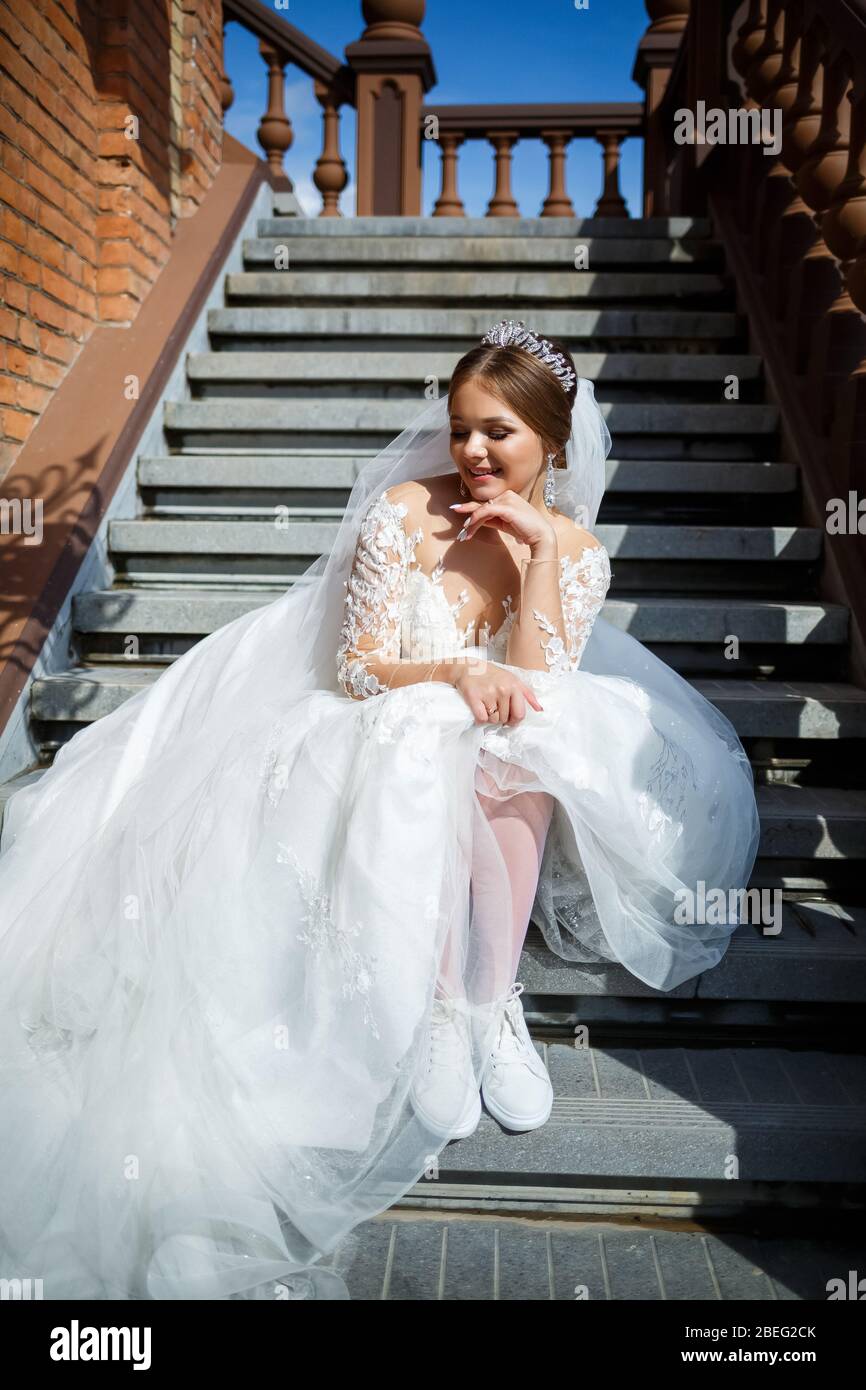 The bride in a white wedding dress and white sneakers sits on the steps of  a large building Stock Photo - Alamy