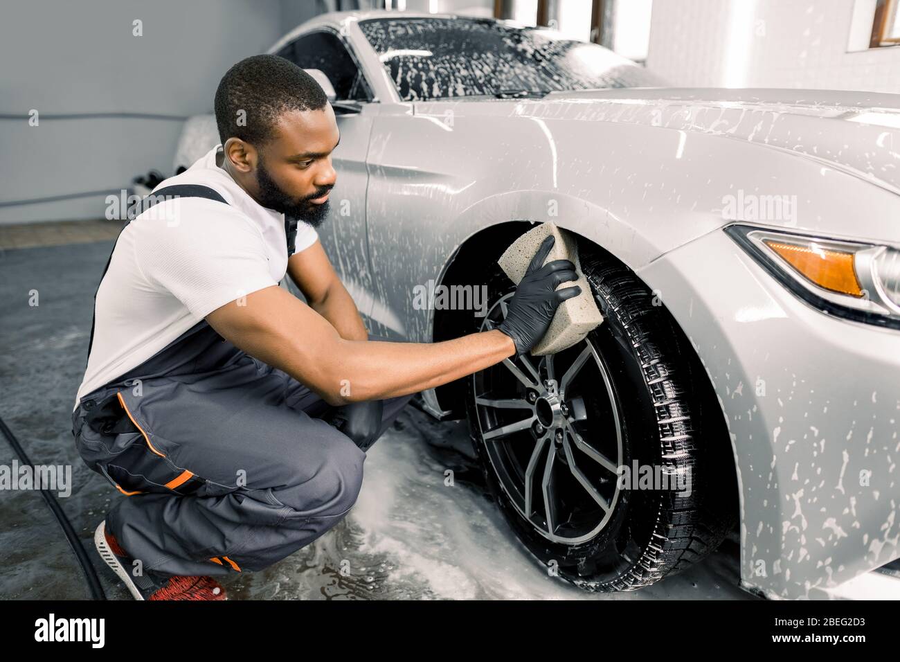 Car washing and detailing photo. African man worker in protective