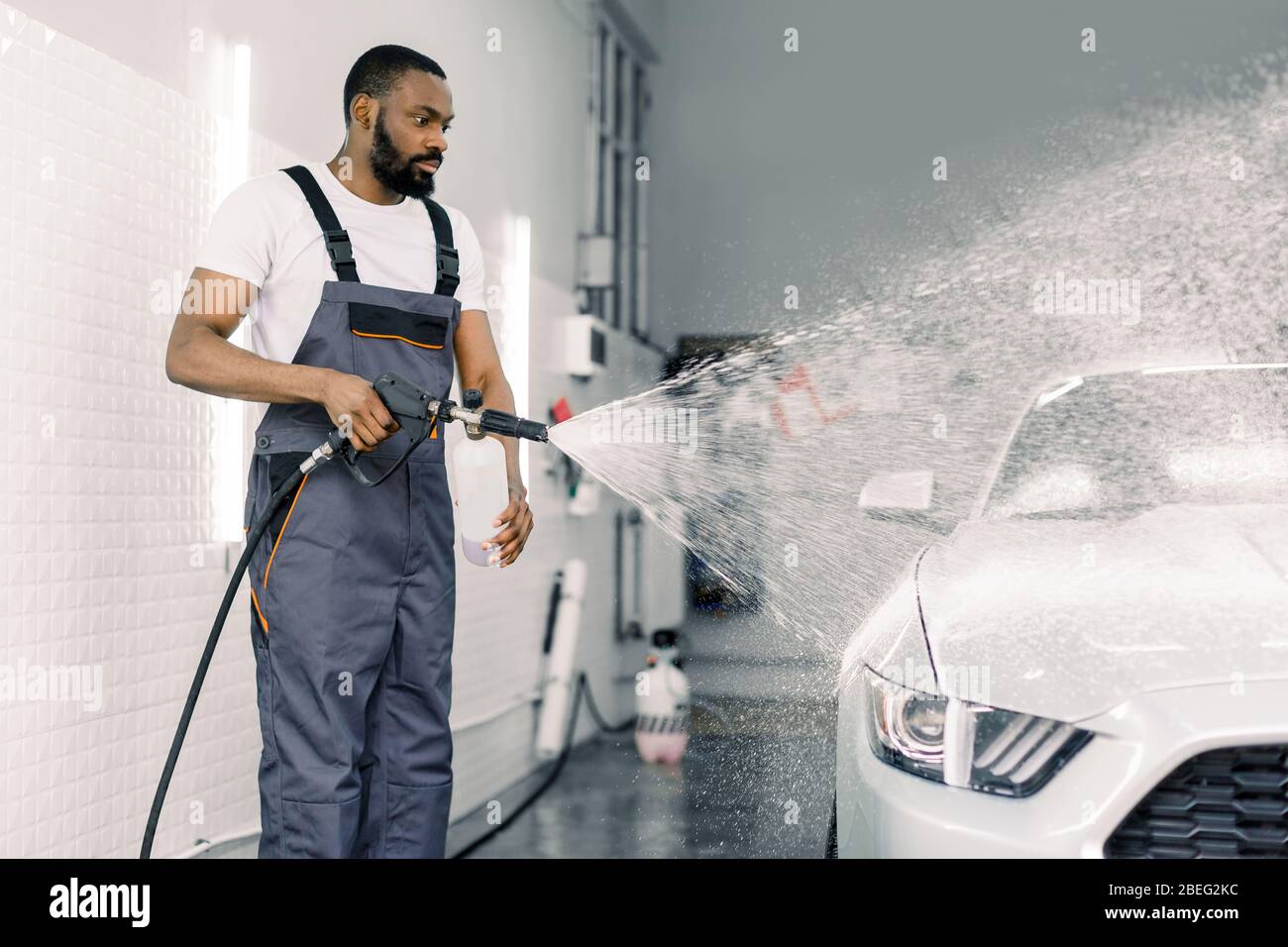 African American man, car wash worker is spraying cleaning foam to