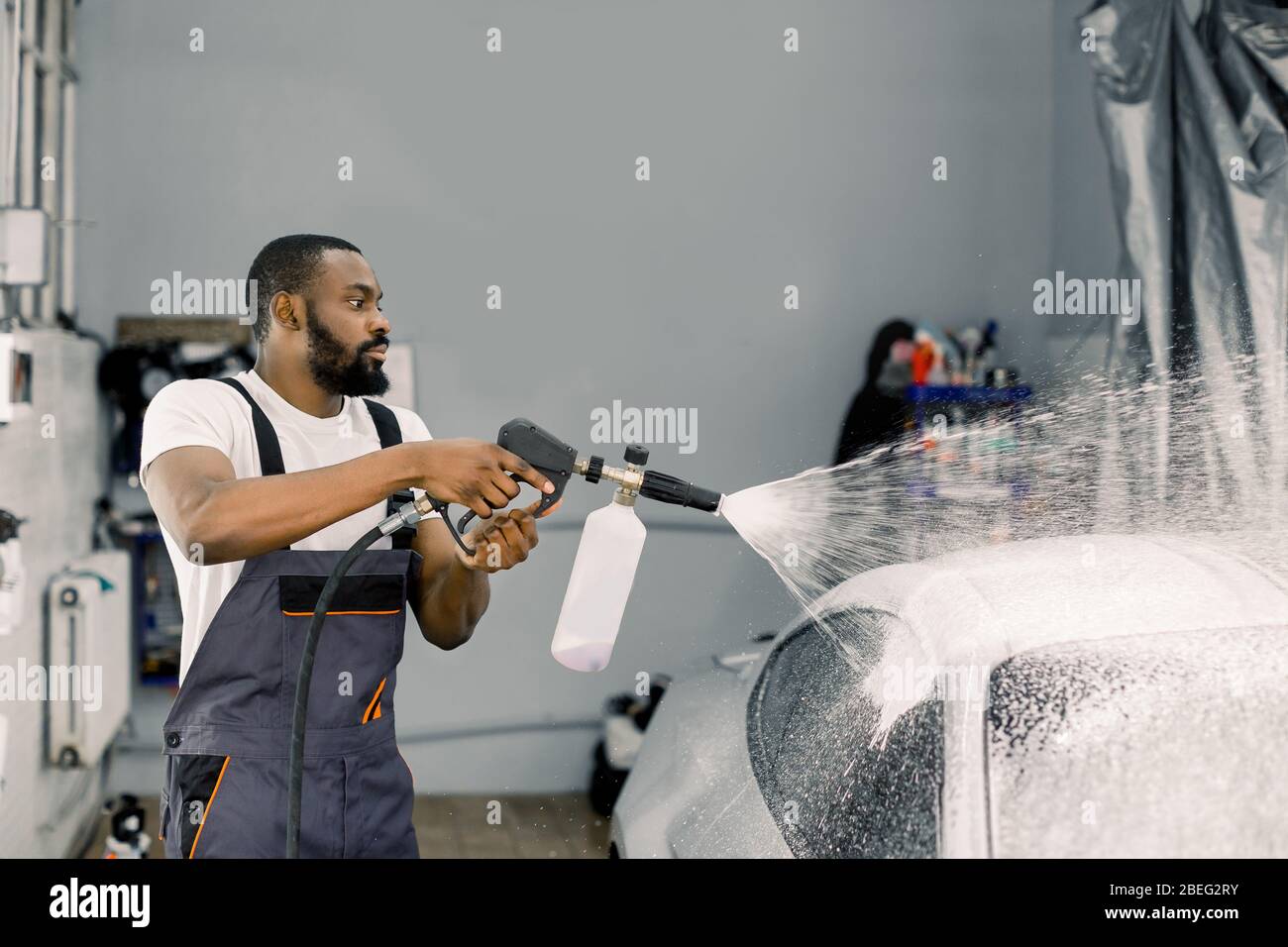 Close up portrait of young pleasant African car wash worker, wearing protective overalls