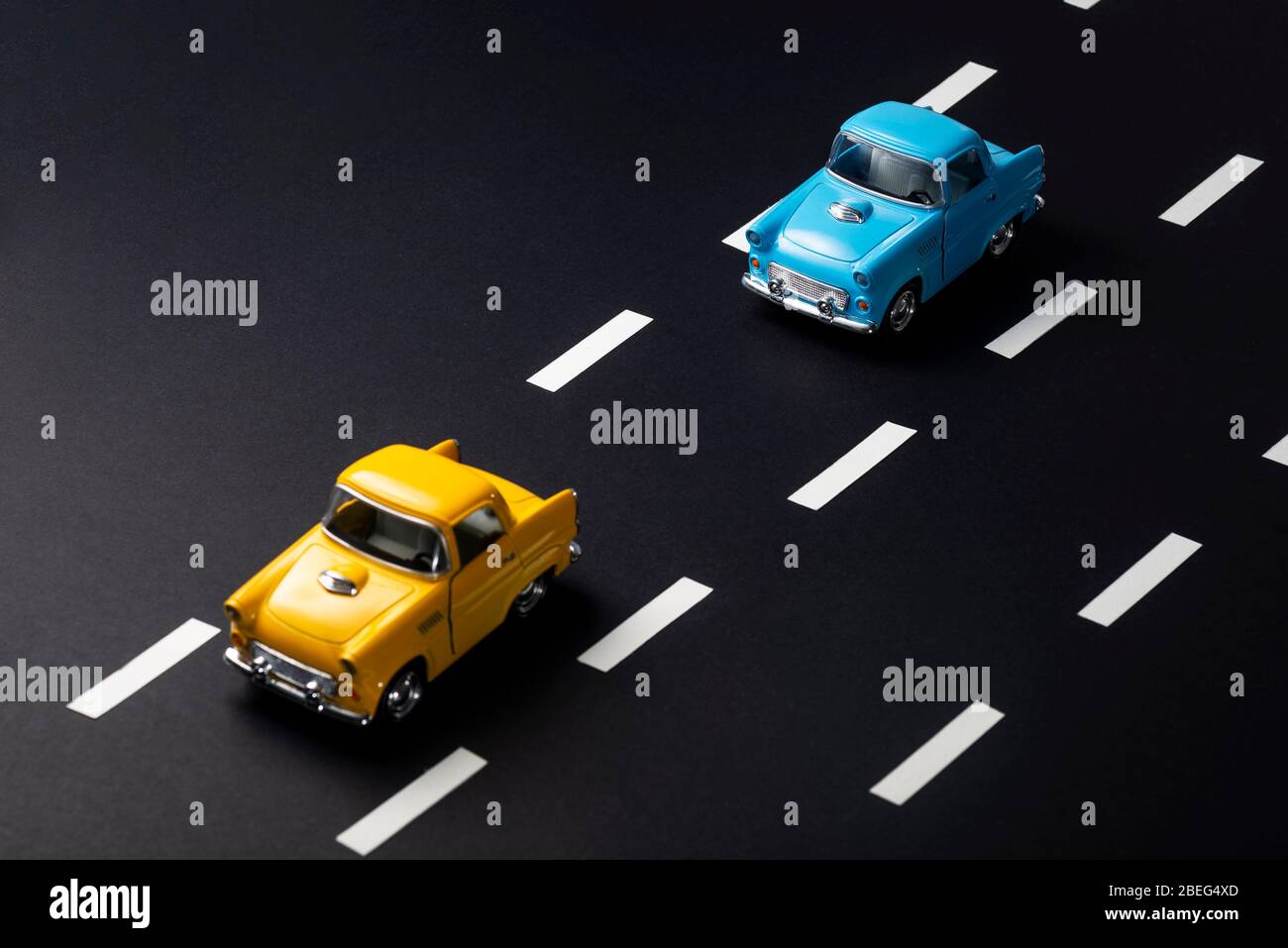 Two toy cars on the road one after another. One is blue one is yellow colored. The image tells about following distance in traffic. Stock Photo