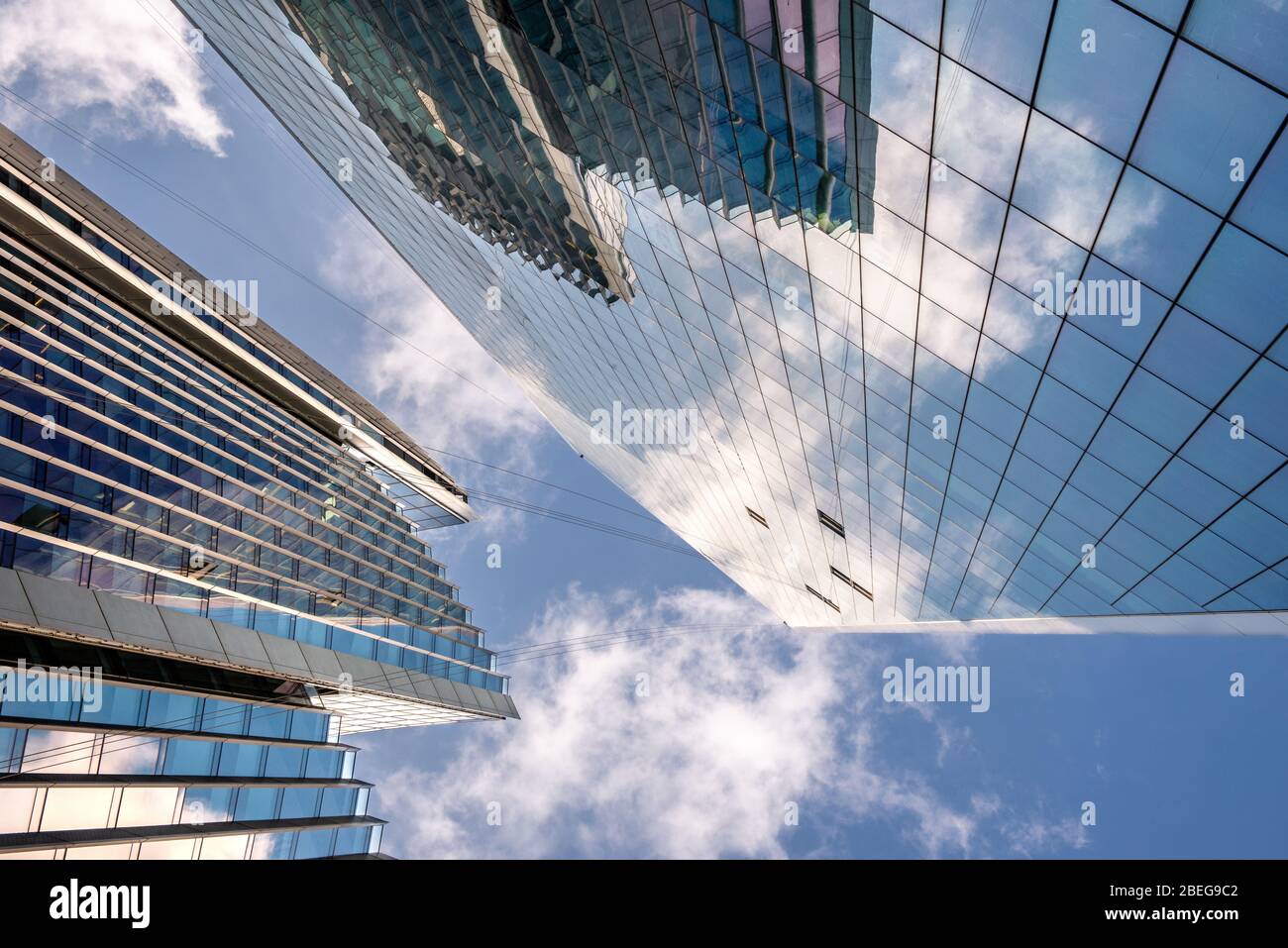 Low angle view of tall corporate glass skyscrapers reflecting a blue sky with white clouds Stock Photo