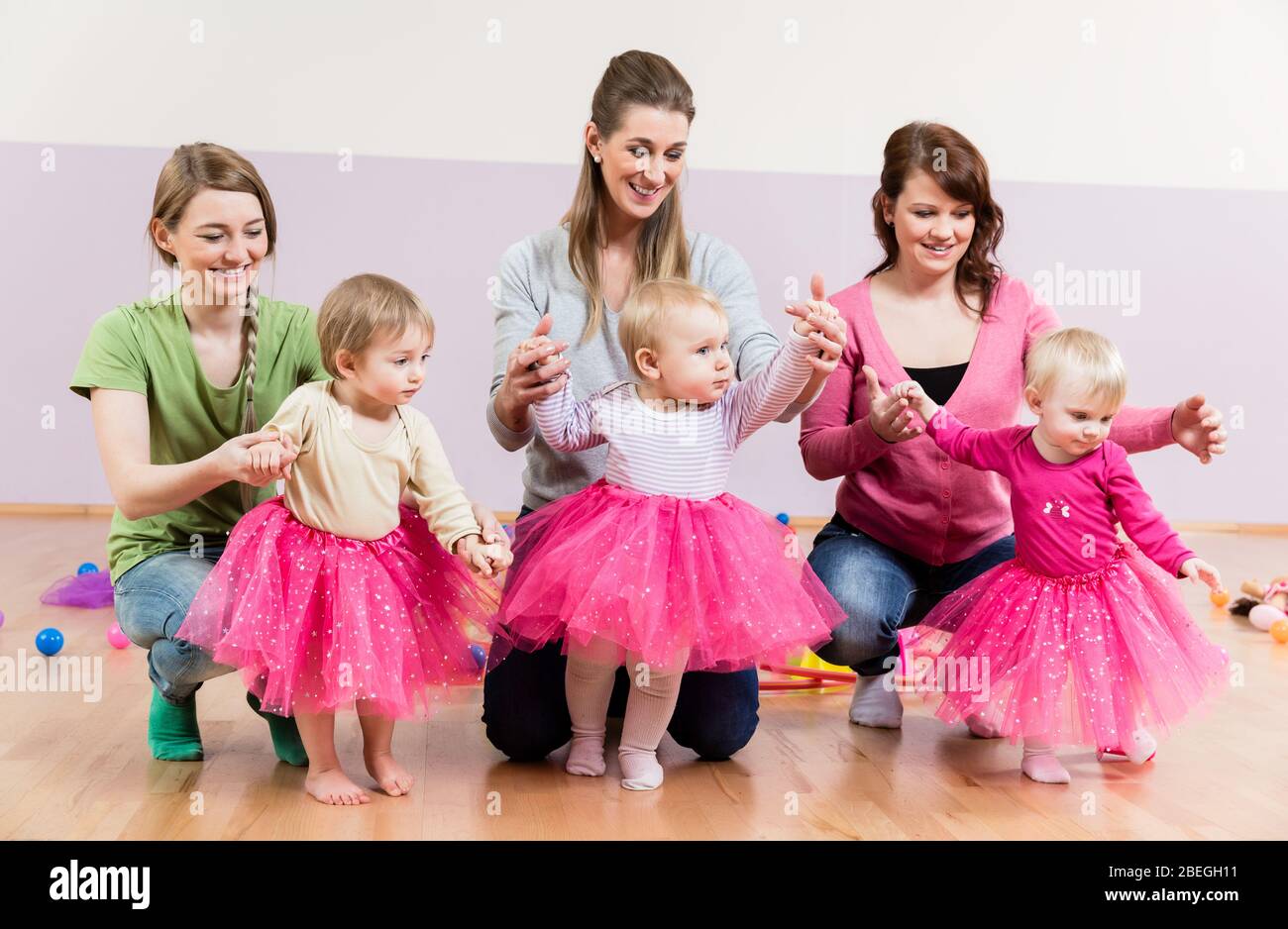 Three baby girls in pink skirts learning to walk Stock Photo