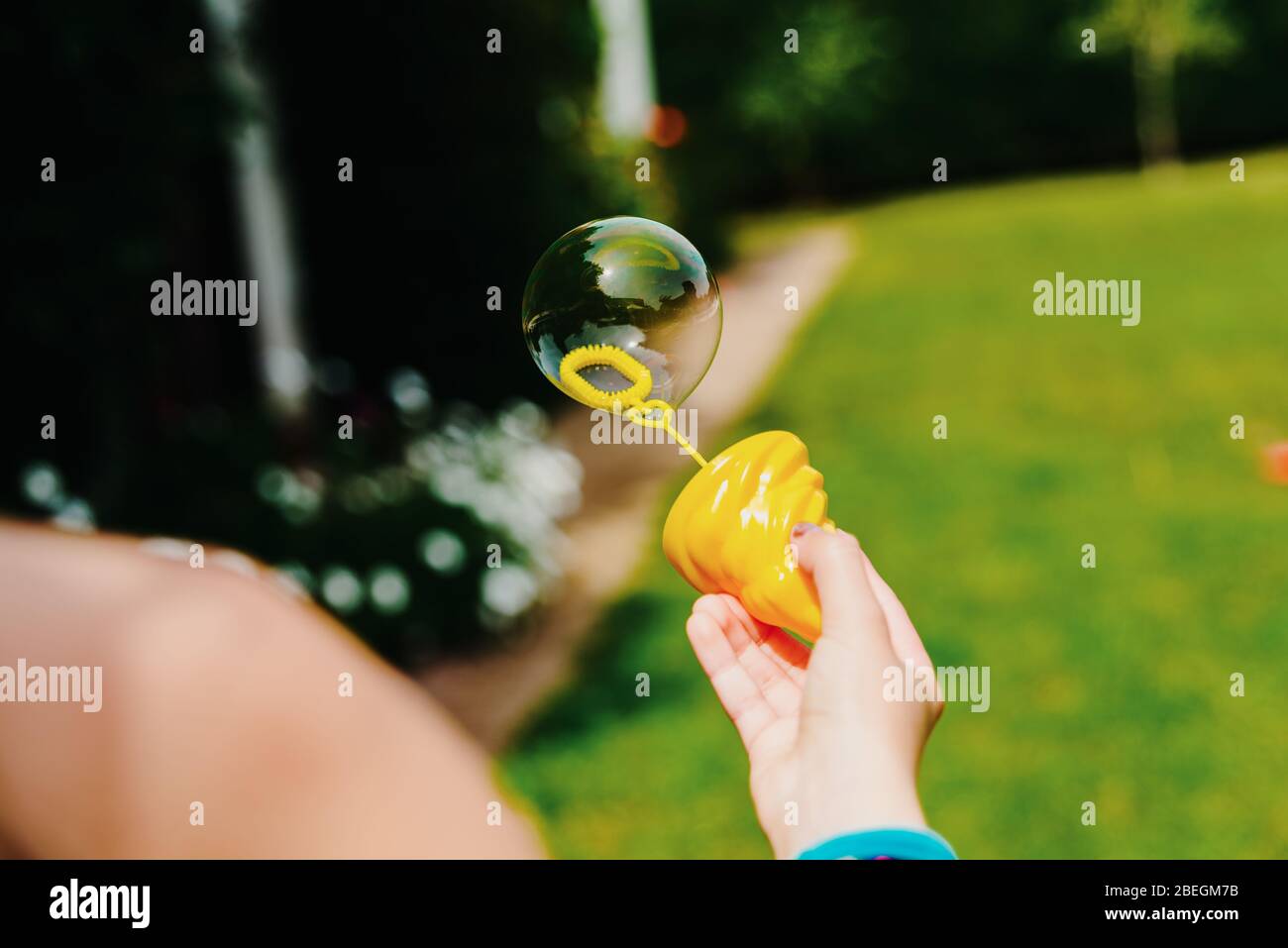 Child's hand holding a soap bubble while playing in summer. Stock Photo