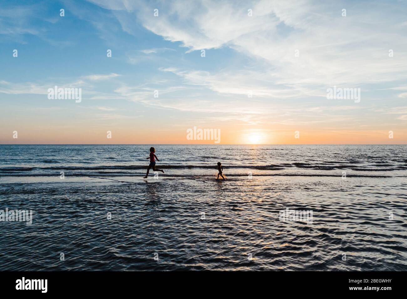 woman and child run in the shallow waters of a florida beach at sunset Stock Photo