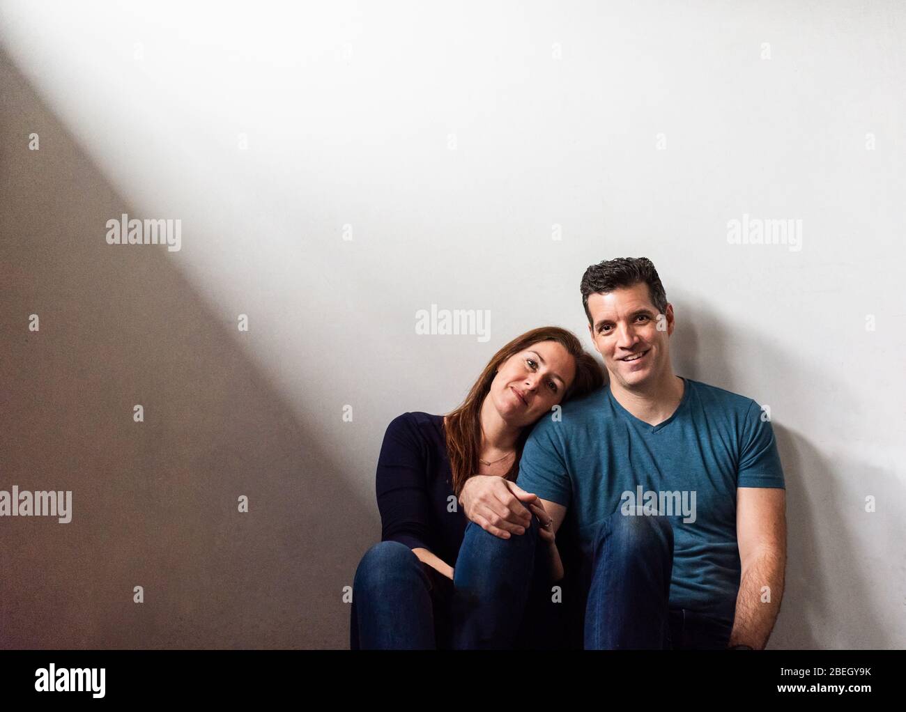 Cropped image of a couple sitting together against a white wall. Stock Photo