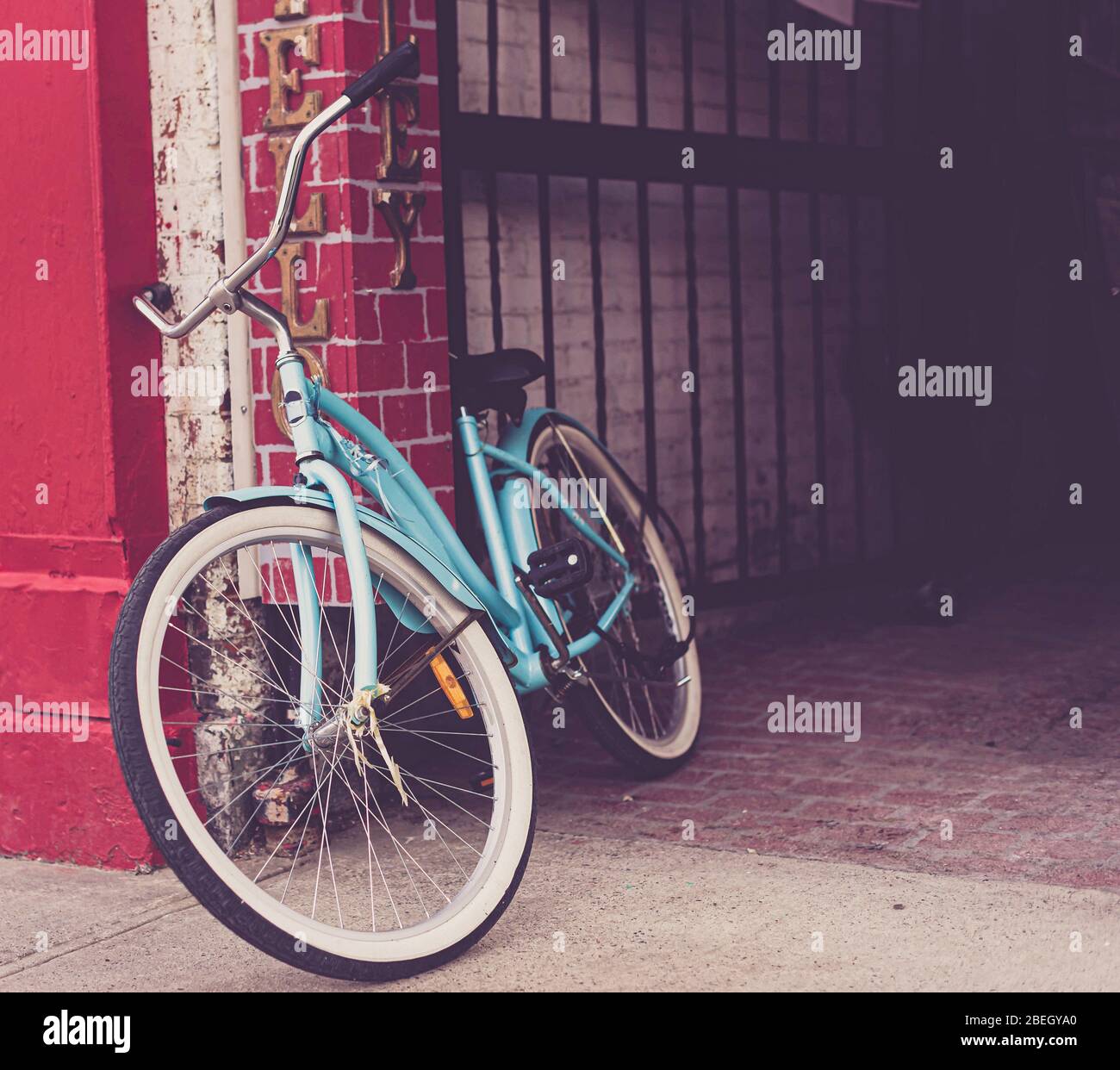 Turquoise blue bicycle leaning against bright red wall near an alley. Stock Photo
