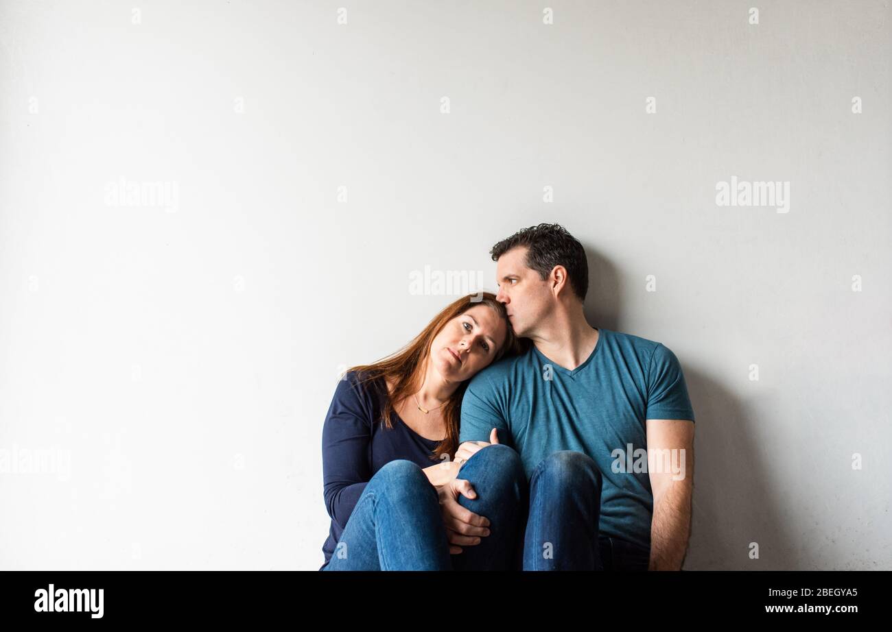 Cropped image of loving couple sitting together against a white wall. Stock Photo