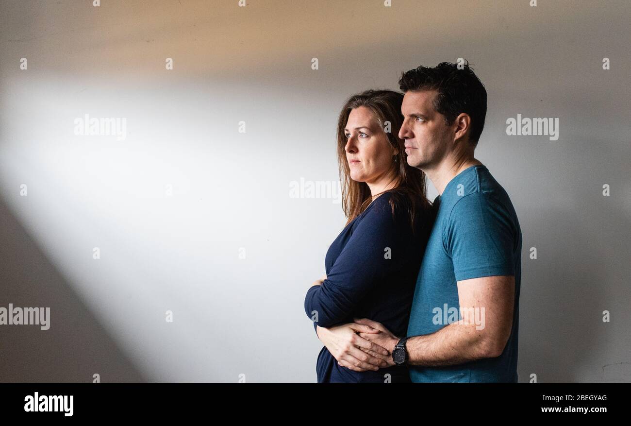 Couple standing close together in a patch of light against white wall. Stock Photo