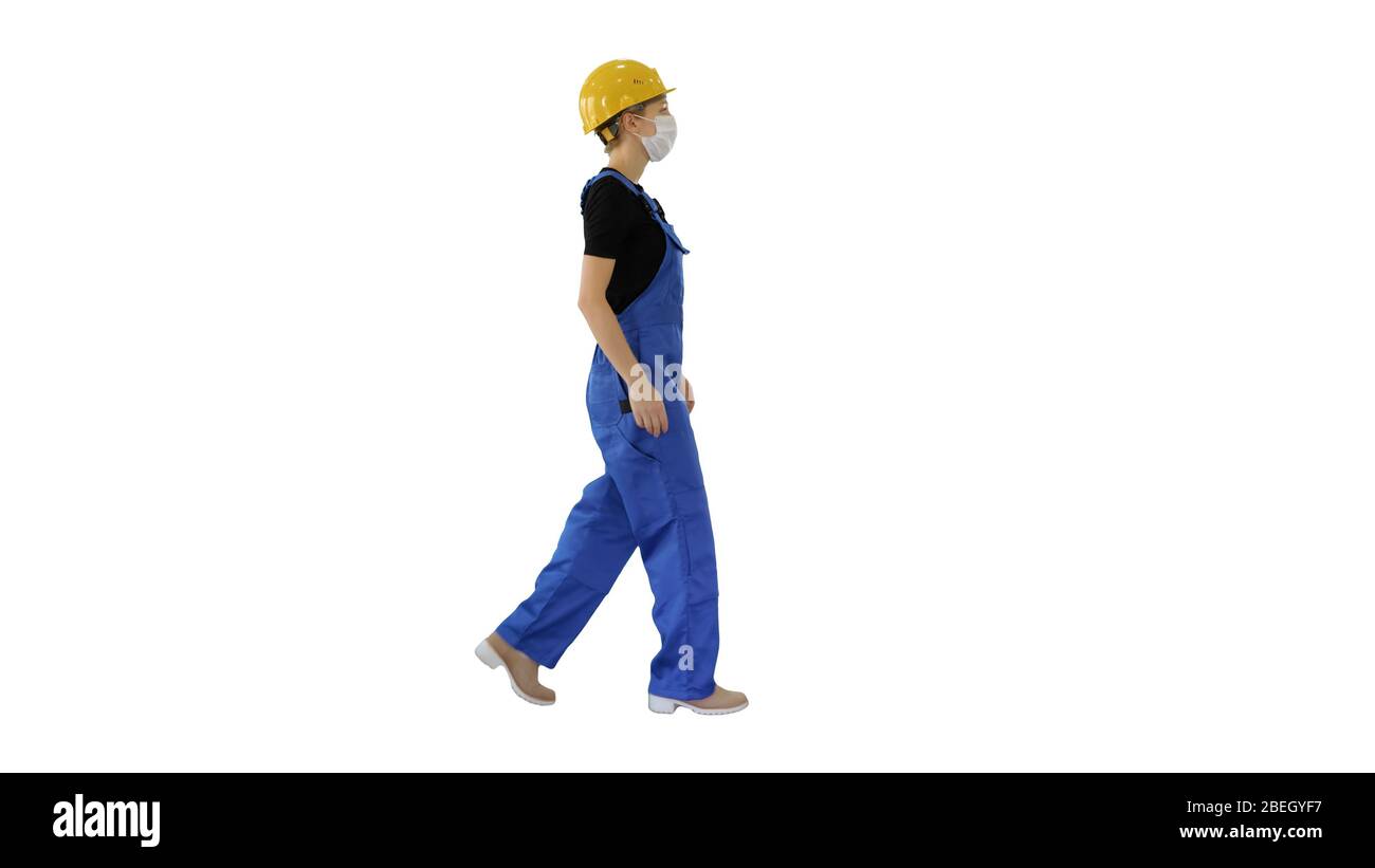 Young woman in hard hat and medical mask walking on white backgr Stock Photo