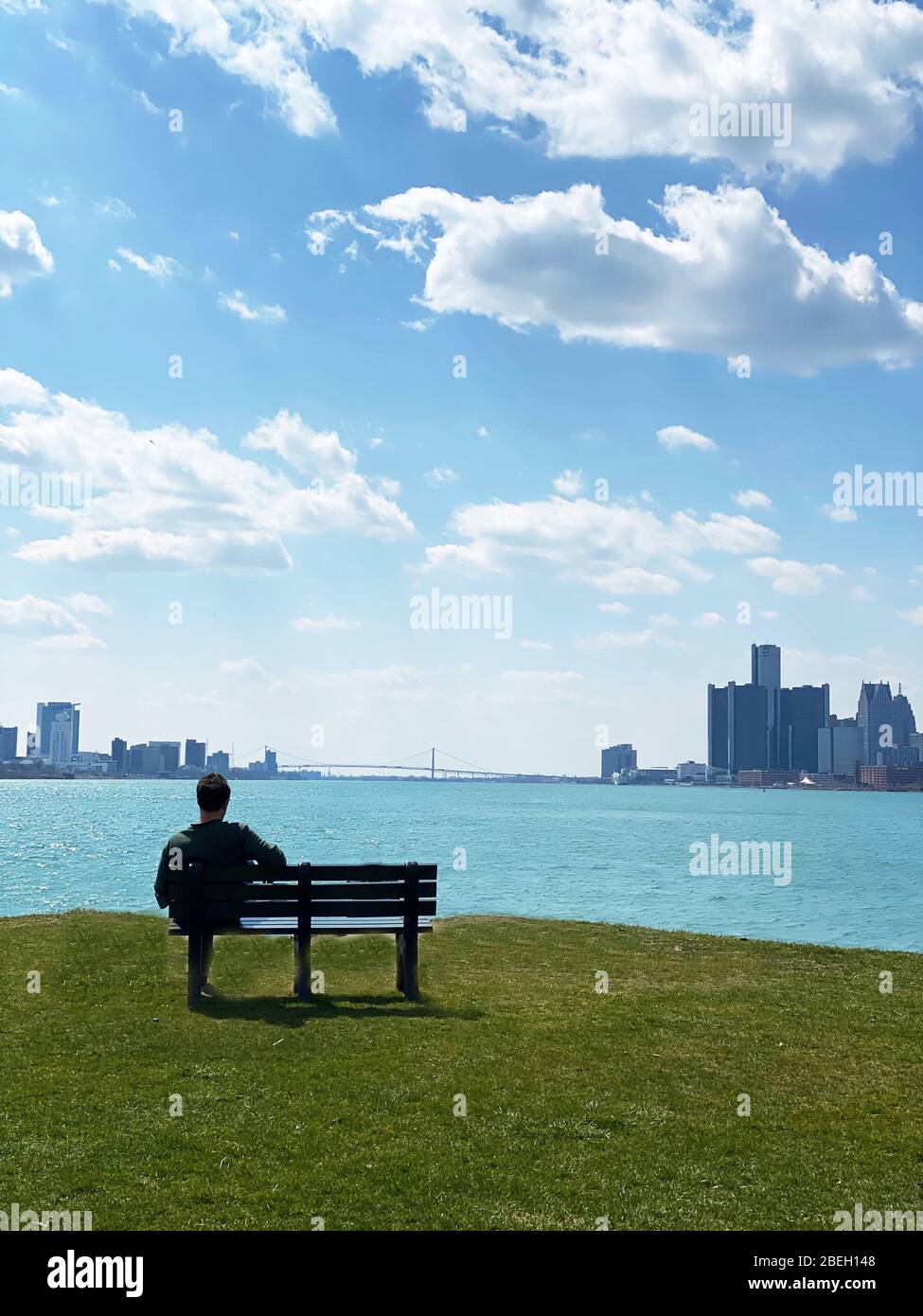 Lone person on bench overlooking Windsor,Canada & Detroit's international border as Social distancing and stay at home order because of Coronavirus Stock Photo
