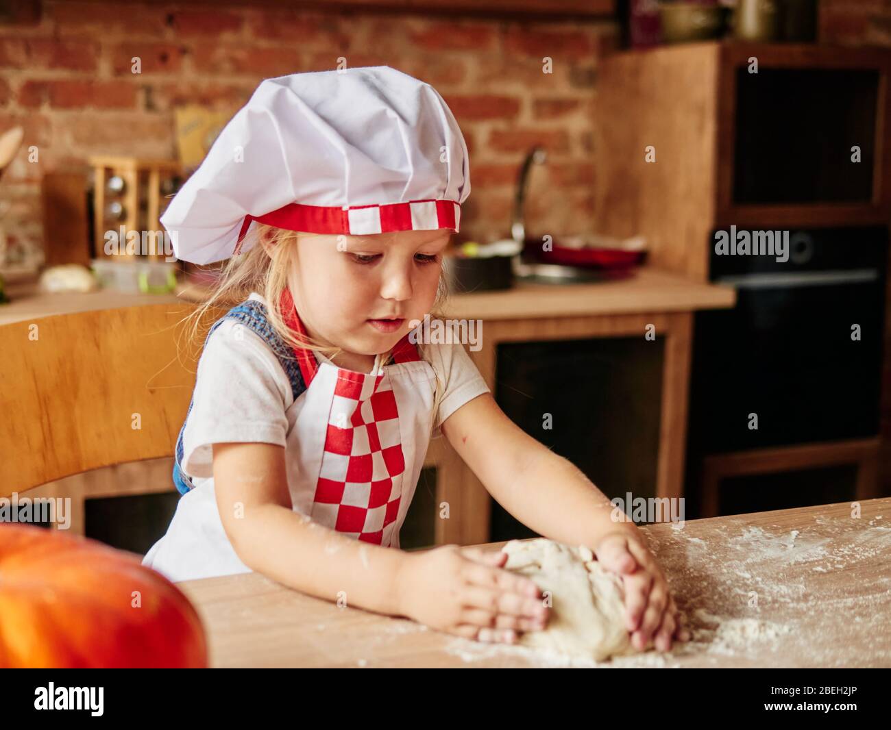 Little girl in cooking chef clothes enjoys kneading the dough. Girls at