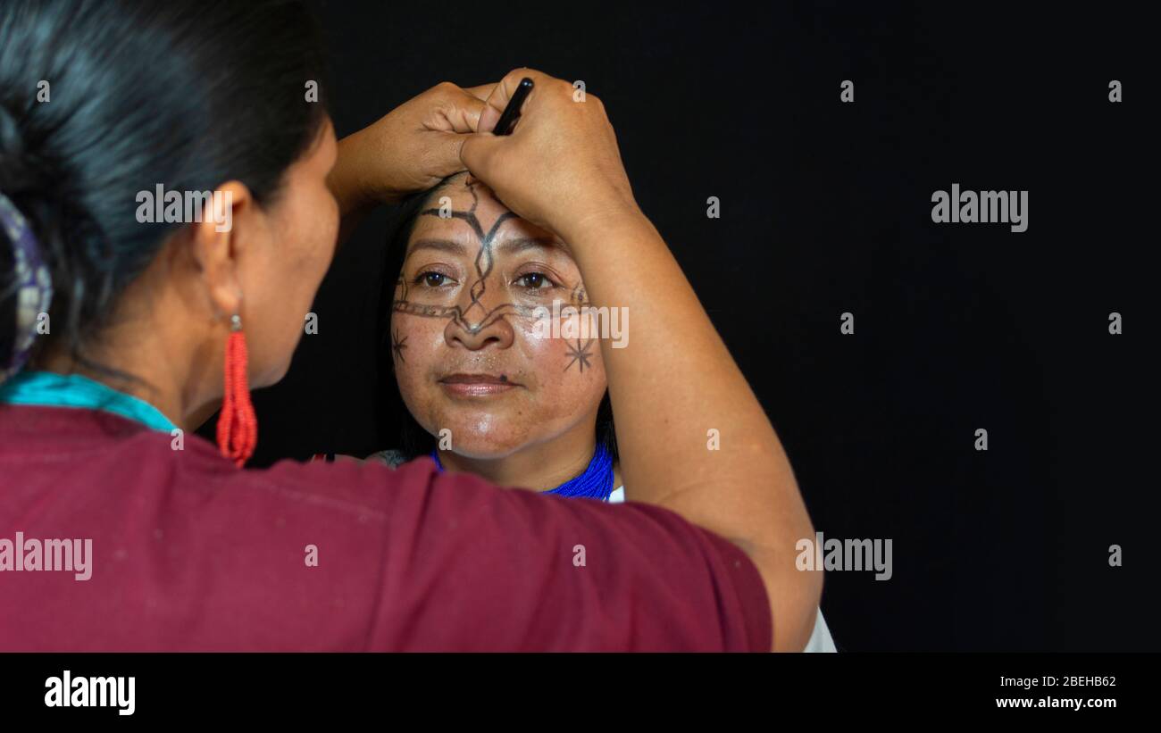 Lago Agrio, Sucumbios / Ecuador - February 29 2020: Woman of the Quichua ethnic group of the Ecuadorian Amazon applying makeup to her sister's face in Stock Photo