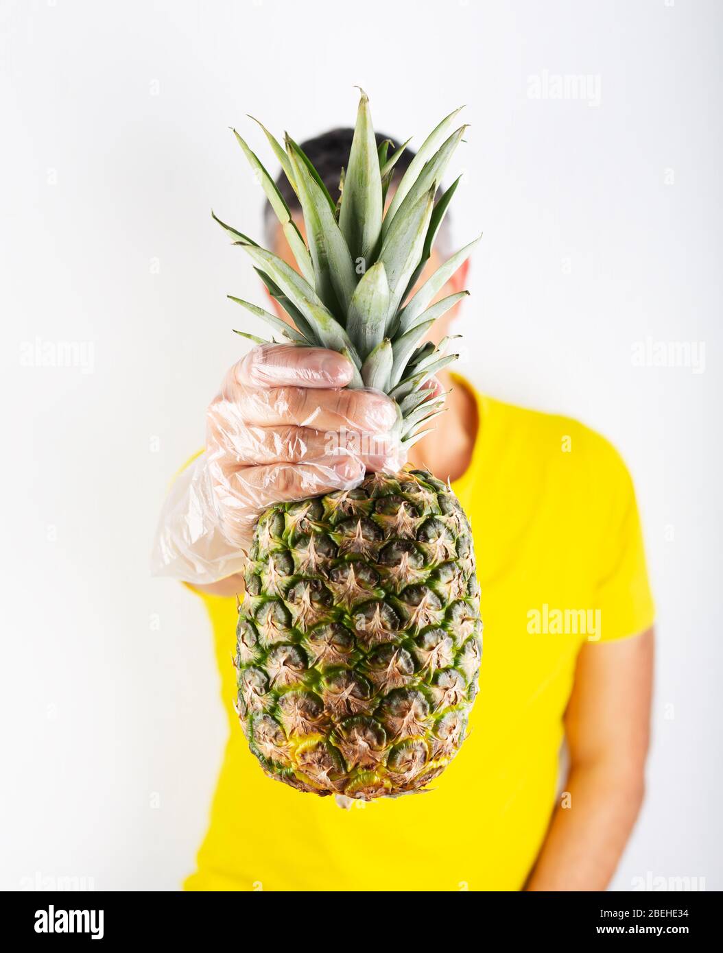 A man in yellow t-shirt wears supermarket gloves and holds ananas. Safety buying Stock Photo