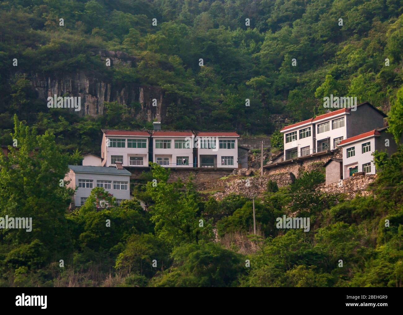 Yichang, China - May 5, 2010: New white houses with red roofs built above cliff on slope of Green foliage covered mountain. Stock Photo