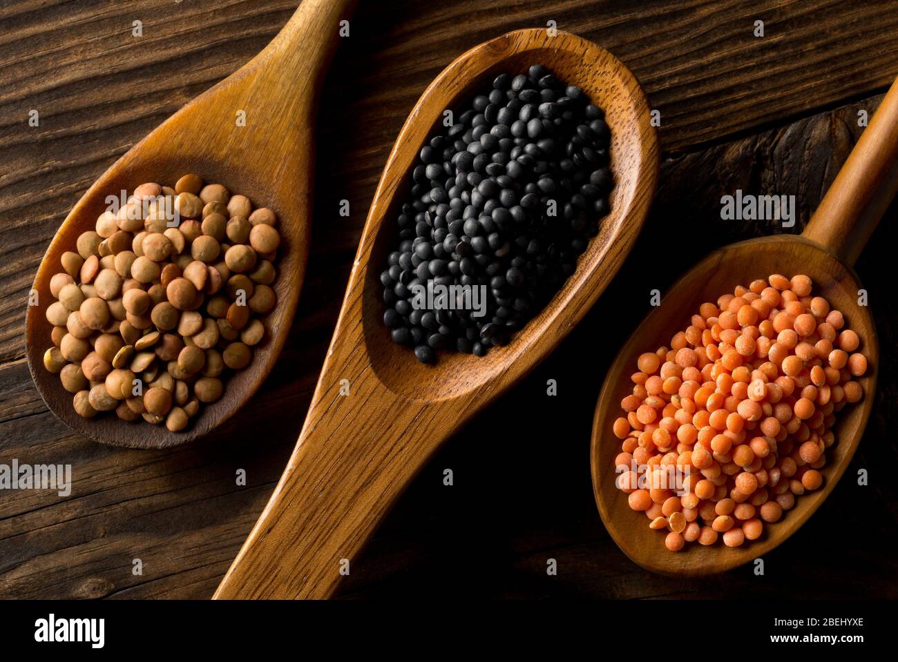 Different assorted lentils mix with red, brown and black beluga lentils in wooden scoops on brown wooden table background top view flat lay from above Stock Photo