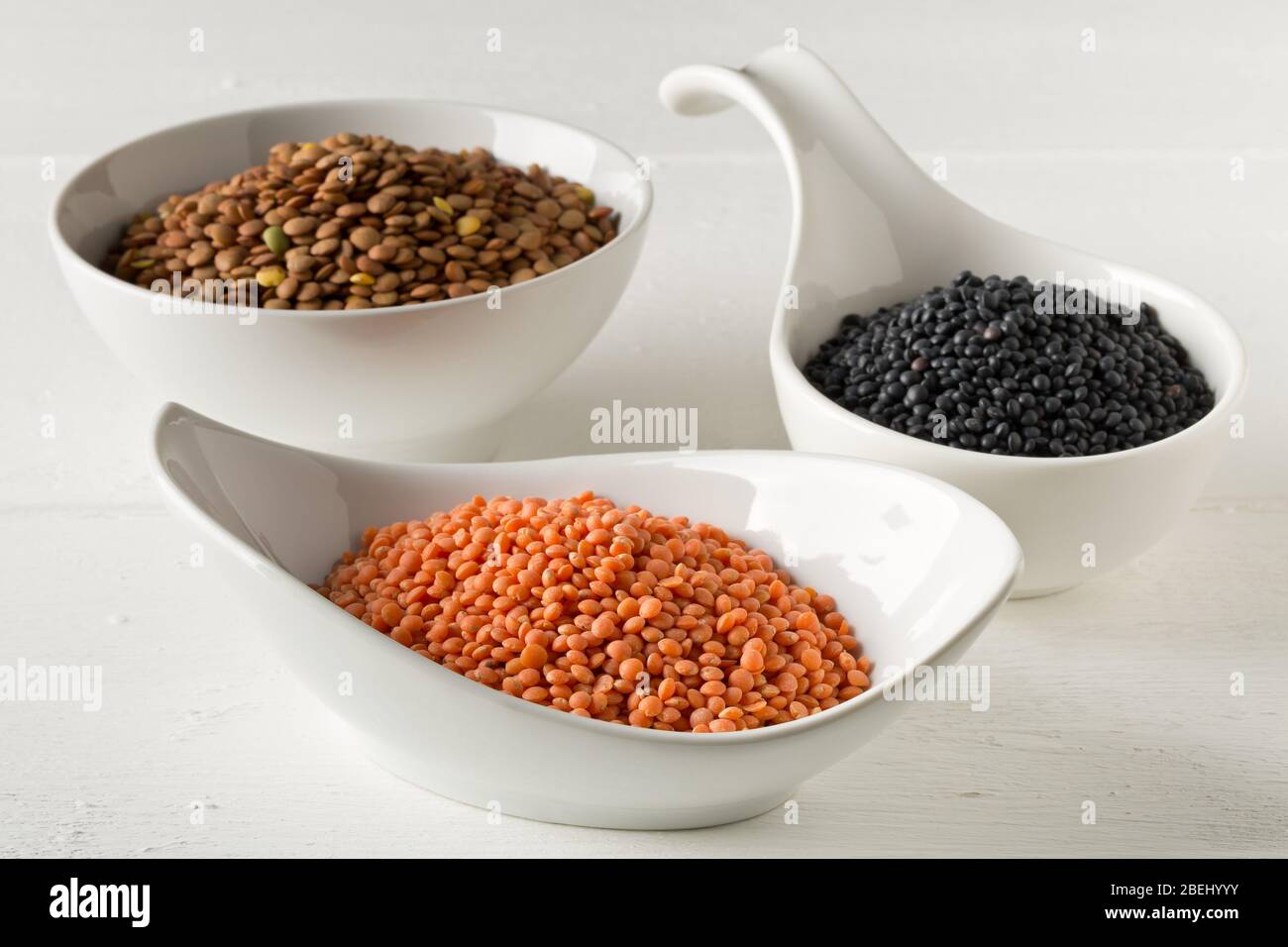 Different assorted lentils mix with red, brown and black beluga lentils in white bowls on white wooden table background - selective focus Stock Photo