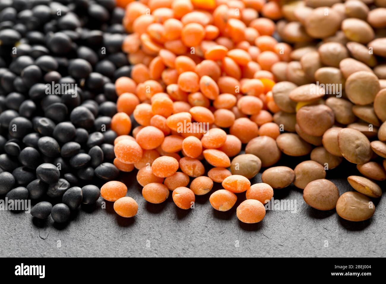 Different assorted lentils mix with red, brown and black beluga lentils on dark stone background macro - selective focus Stock Photo
