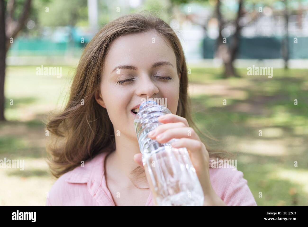 Young caucasian woman girl drinking water from a plastic bottle in green park, close up Stock Photo