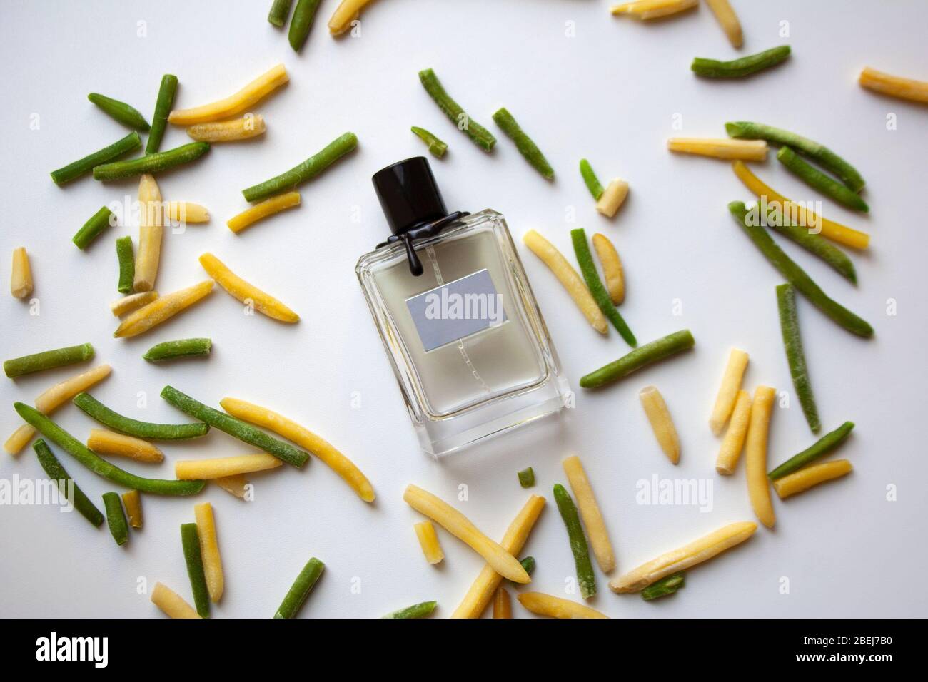 Glass perfume bottle with green and yellow bean pods on white background Stock Photo