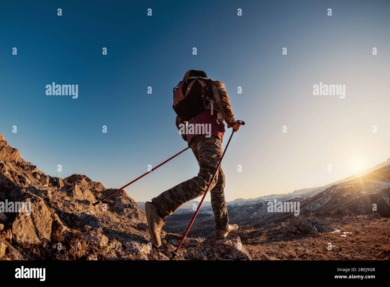 Hiker with backpack walks or explores the mountains at sunset time Stock Photo