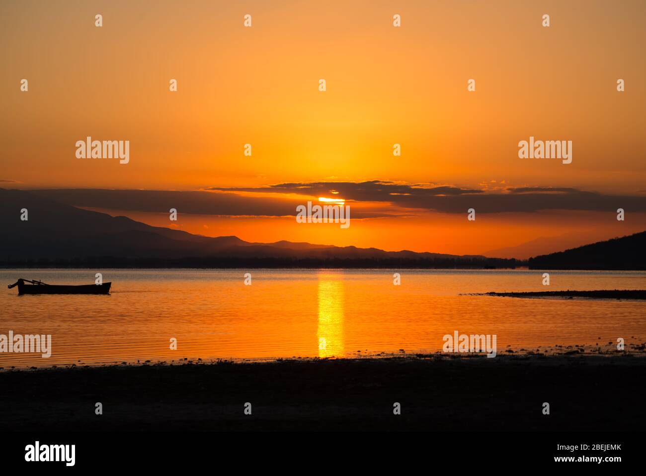 Beautiful orange sunrise over the clam lake with boat silhouette Background. Stock Photo