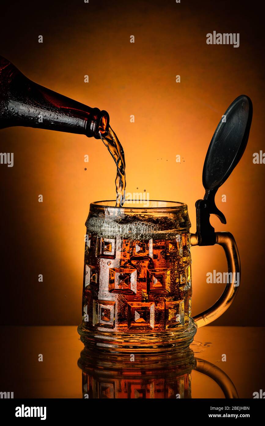 fresh beer poured from the bottle into the glass mug on the golden background Stock Photo