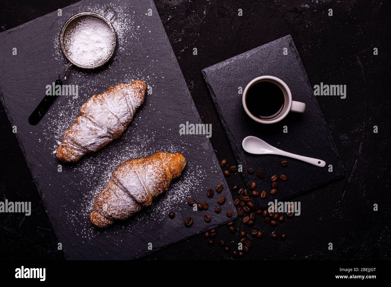 top view, cup of black coffee and croissants with veiled sugar on a dark background Stock Photo