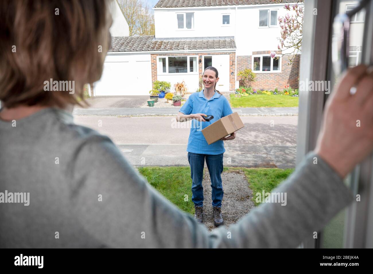 Female Delivery Driver Leaving Package Outside House For Safety Observing Social Distancing During Coronavirus Pandemic Stock Photo